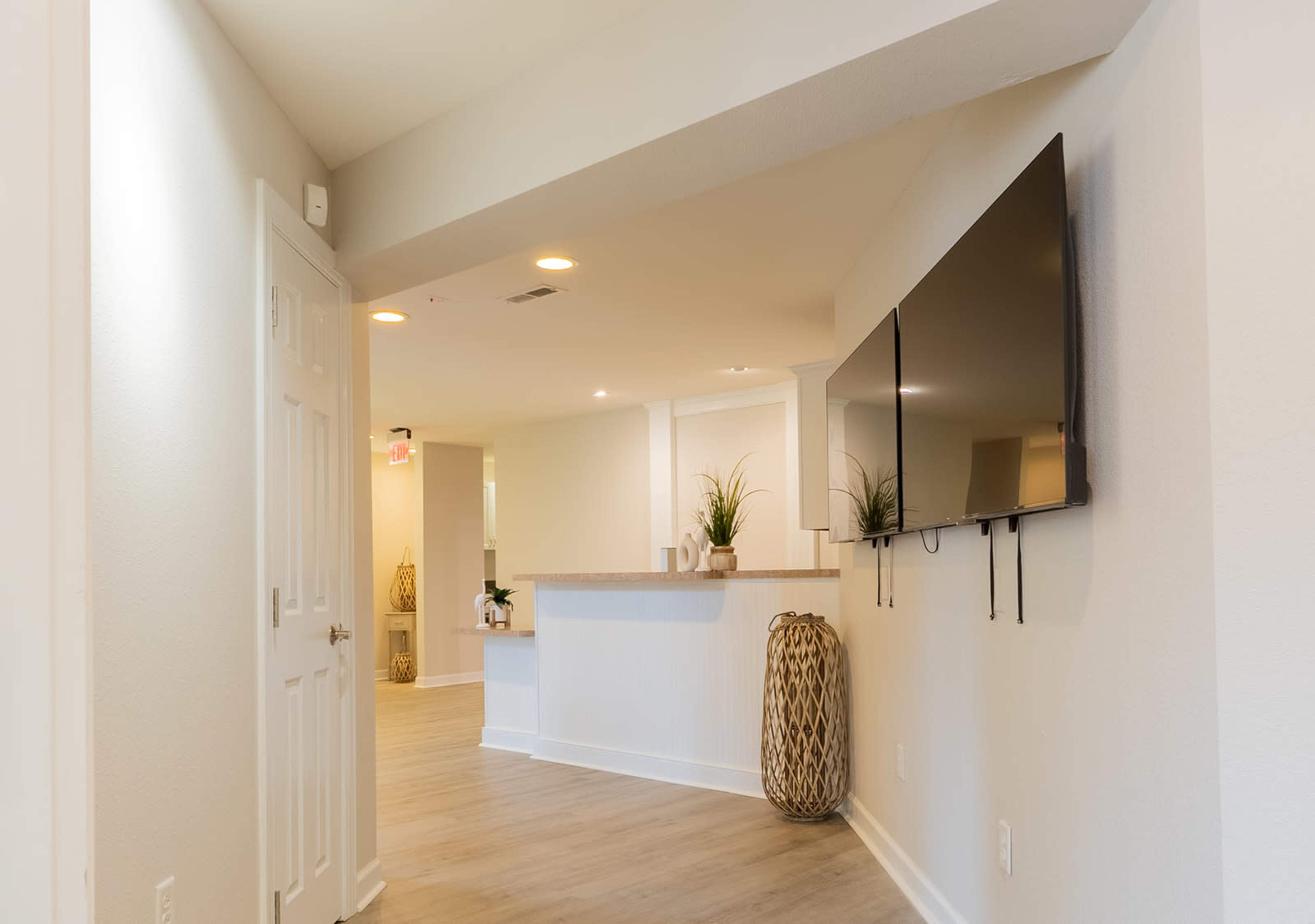 A well-lit hallway leading to a reception area with a wall-mounted television and a countertop.