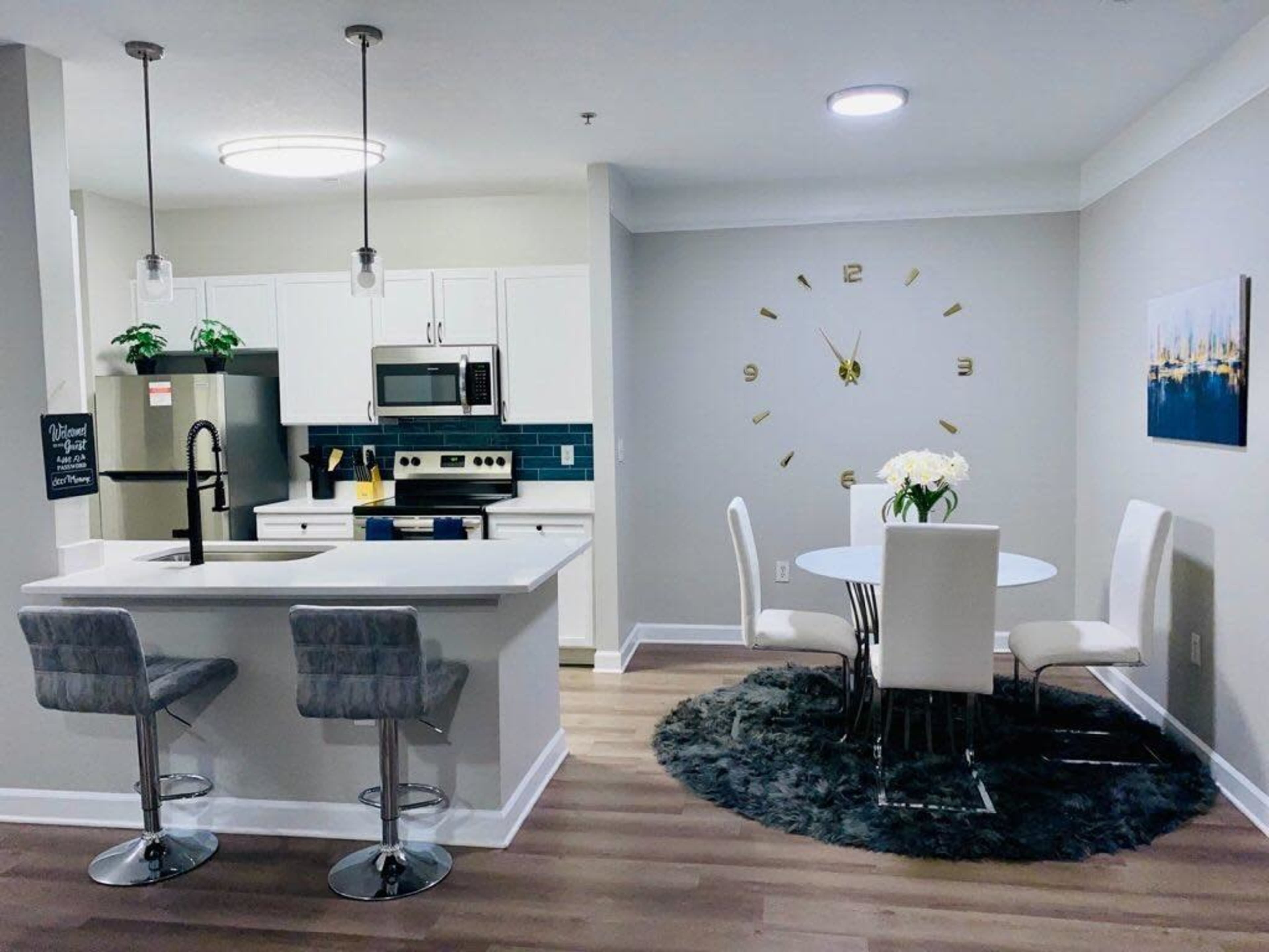 A modern kitchen and dining area featuring stainless steel appliances, a round dining table with white chairs, and a circular rug on a wooden floor.