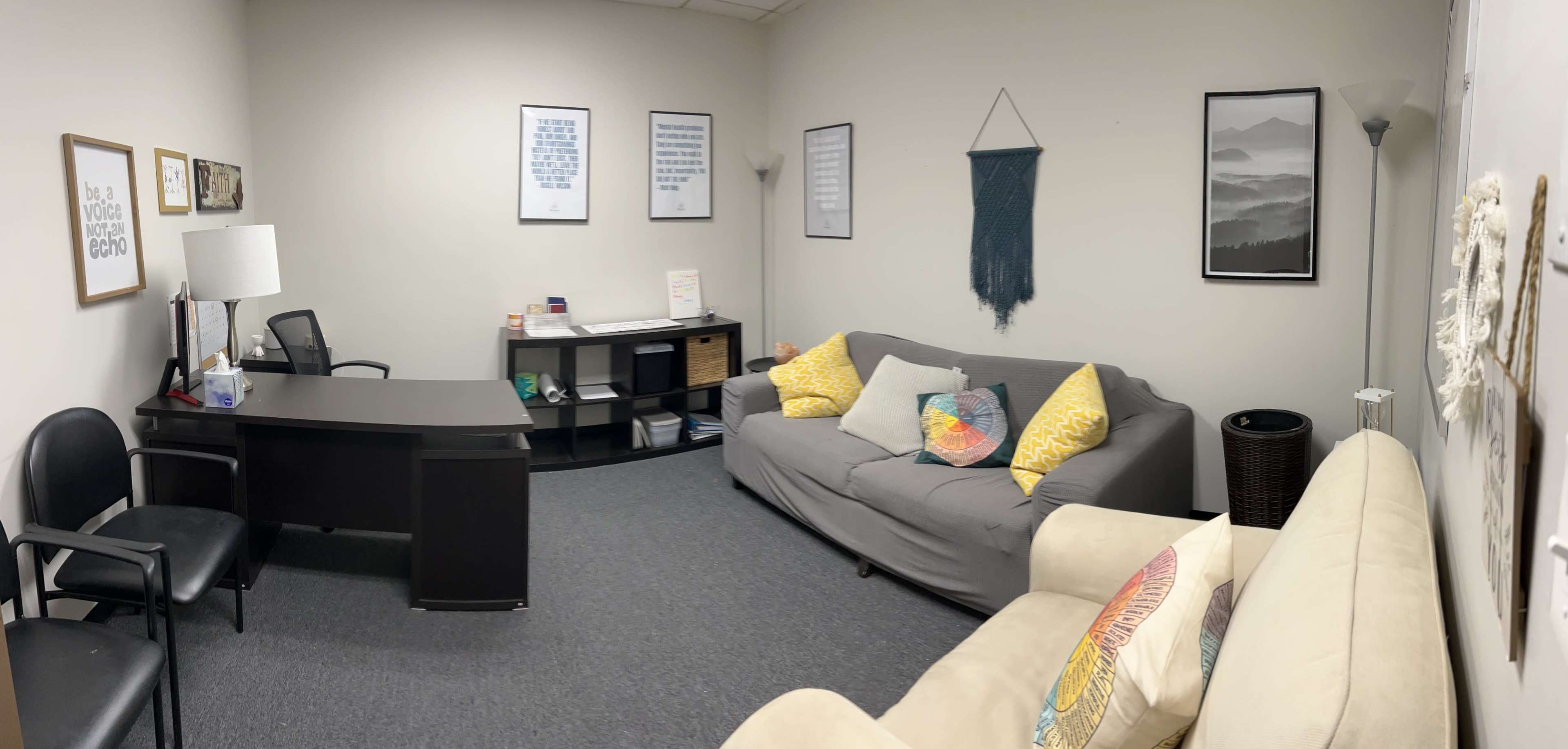 The image shows a modern office waiting room with two sofas, a desk, shelves, and framed artwork on the walls.