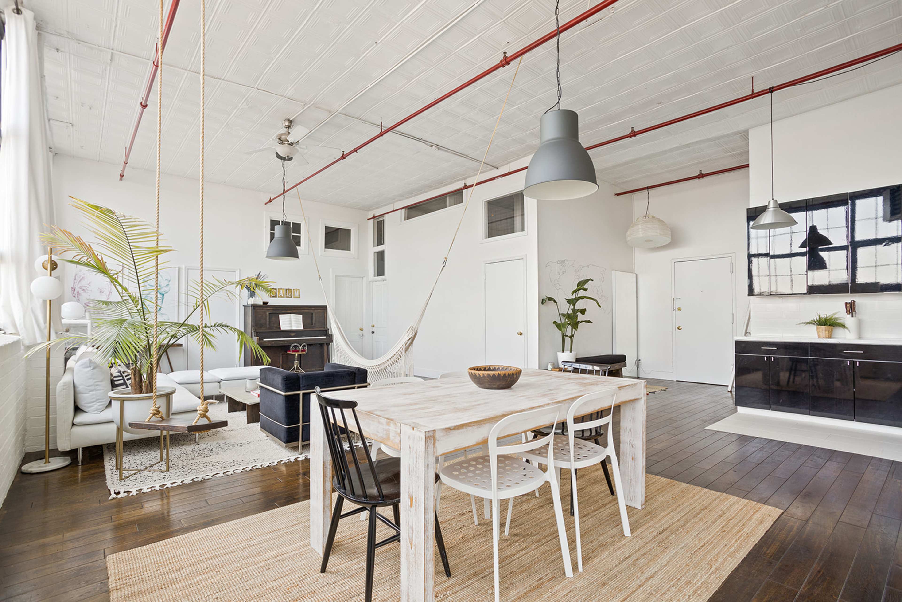 A bright, spacious room with a dining table surrounded by chairs, a sofa area, and a kitchen in the background.