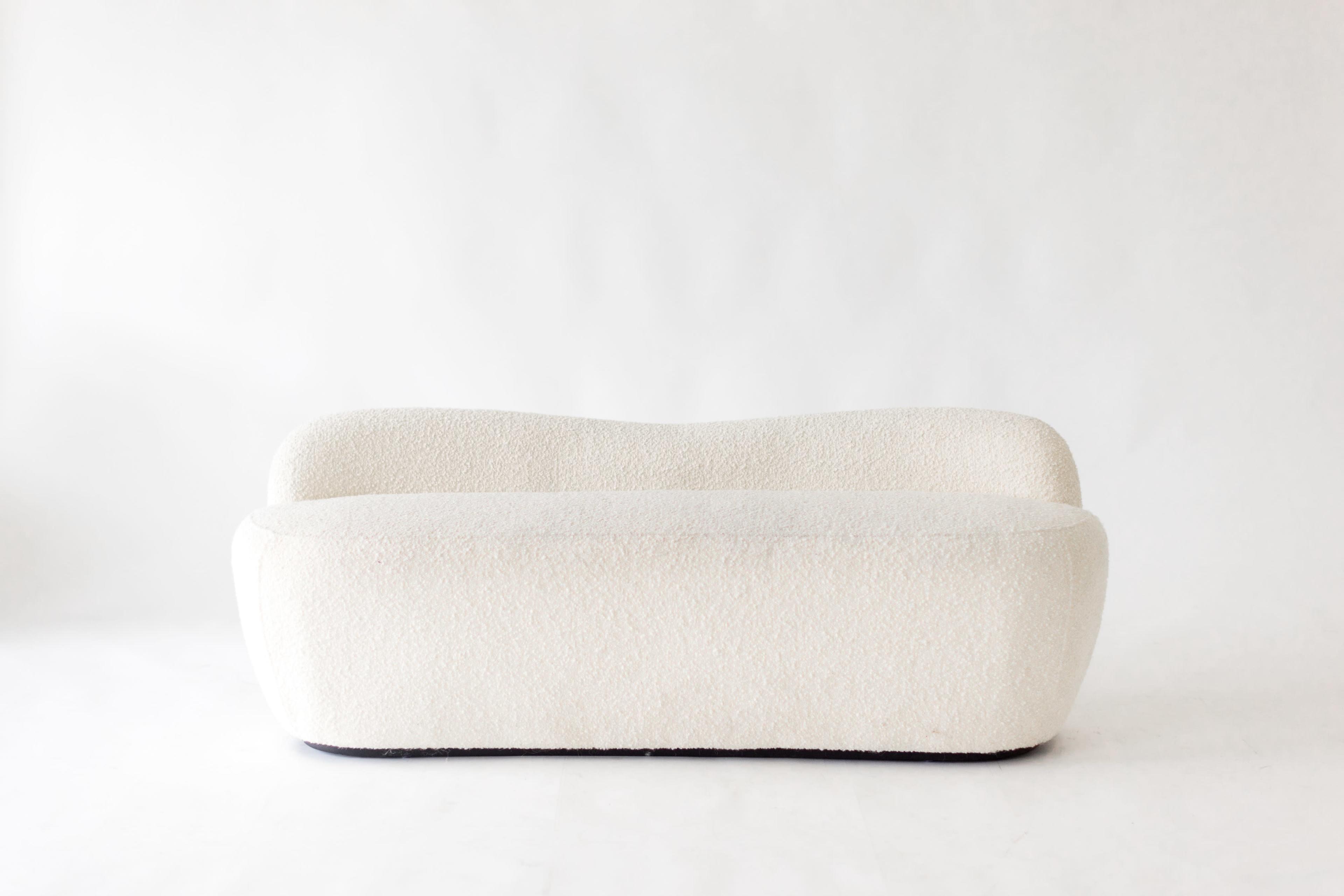 A white, rounded sofa with a textured fabric sits against a plain background.