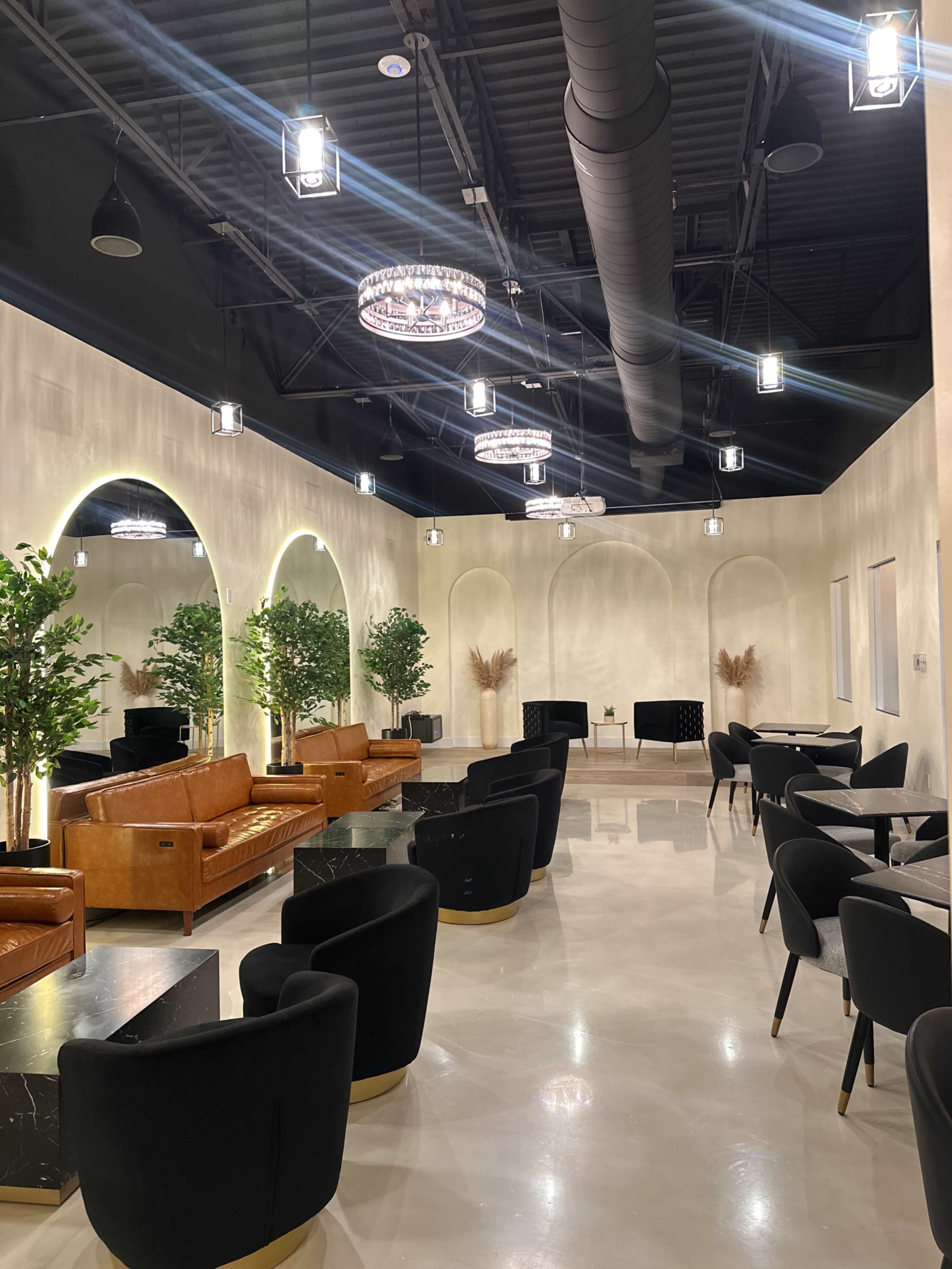 The image shows a modern lounge area featuring leather sofas, black chairs, and decorative plants against a softly lit, neutral-toned wall.