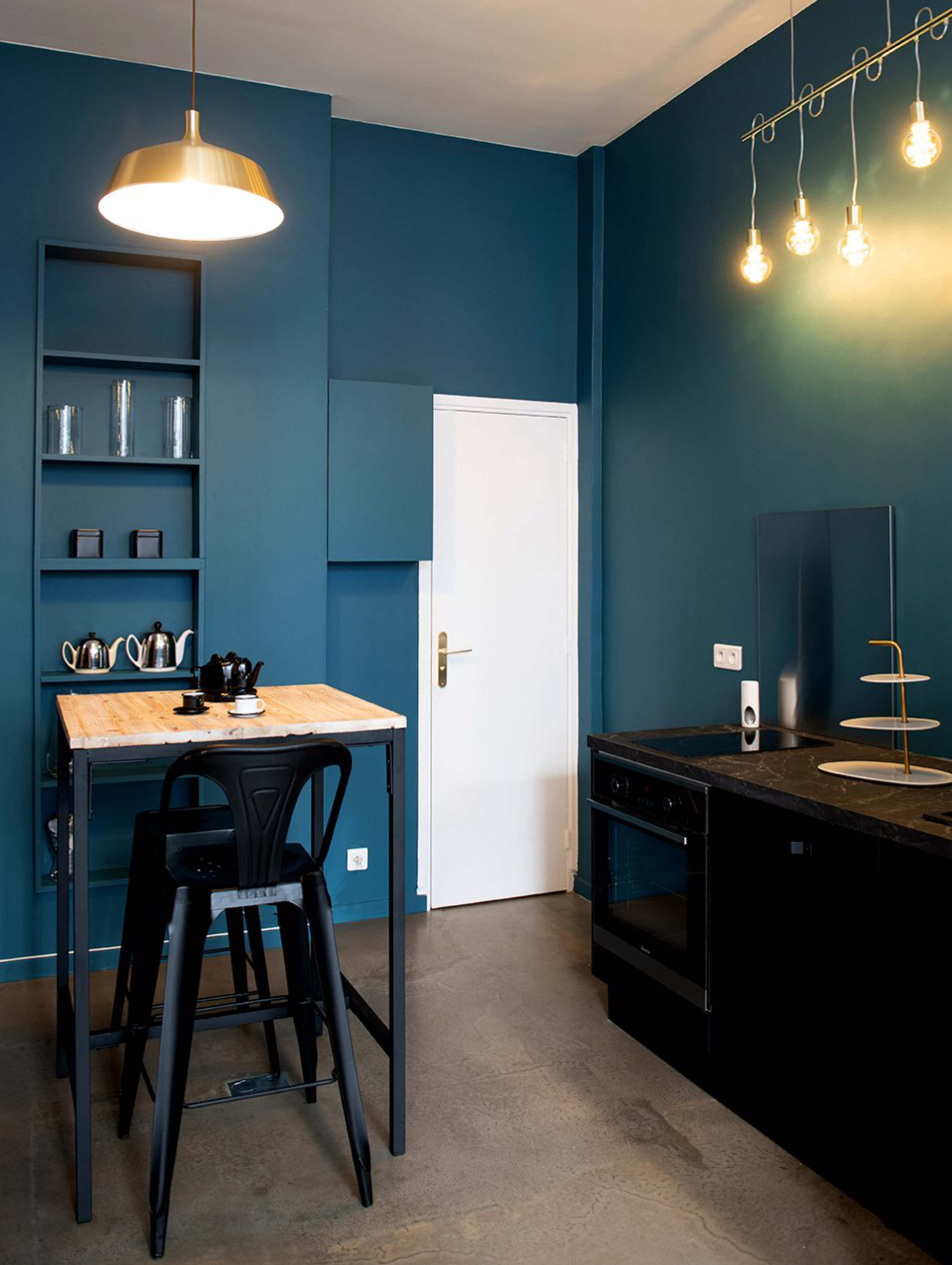 A modern kitchen with a blue wall, a wooden table with black stools, and sleek black cabinets and appliances.