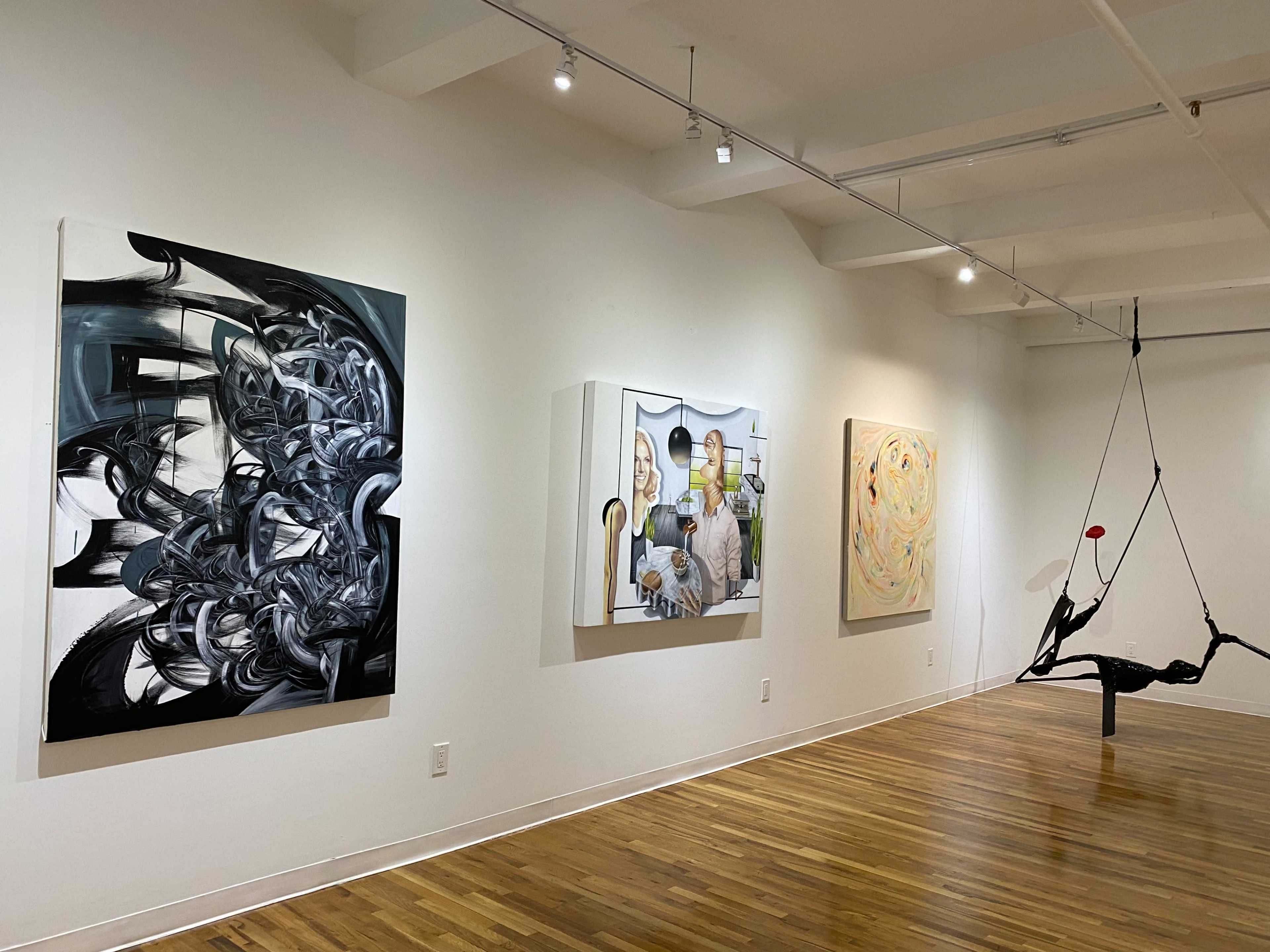 An art gallery featuring four distinct artworks on the white walls and a sculptural piece hanging from the ceiling.