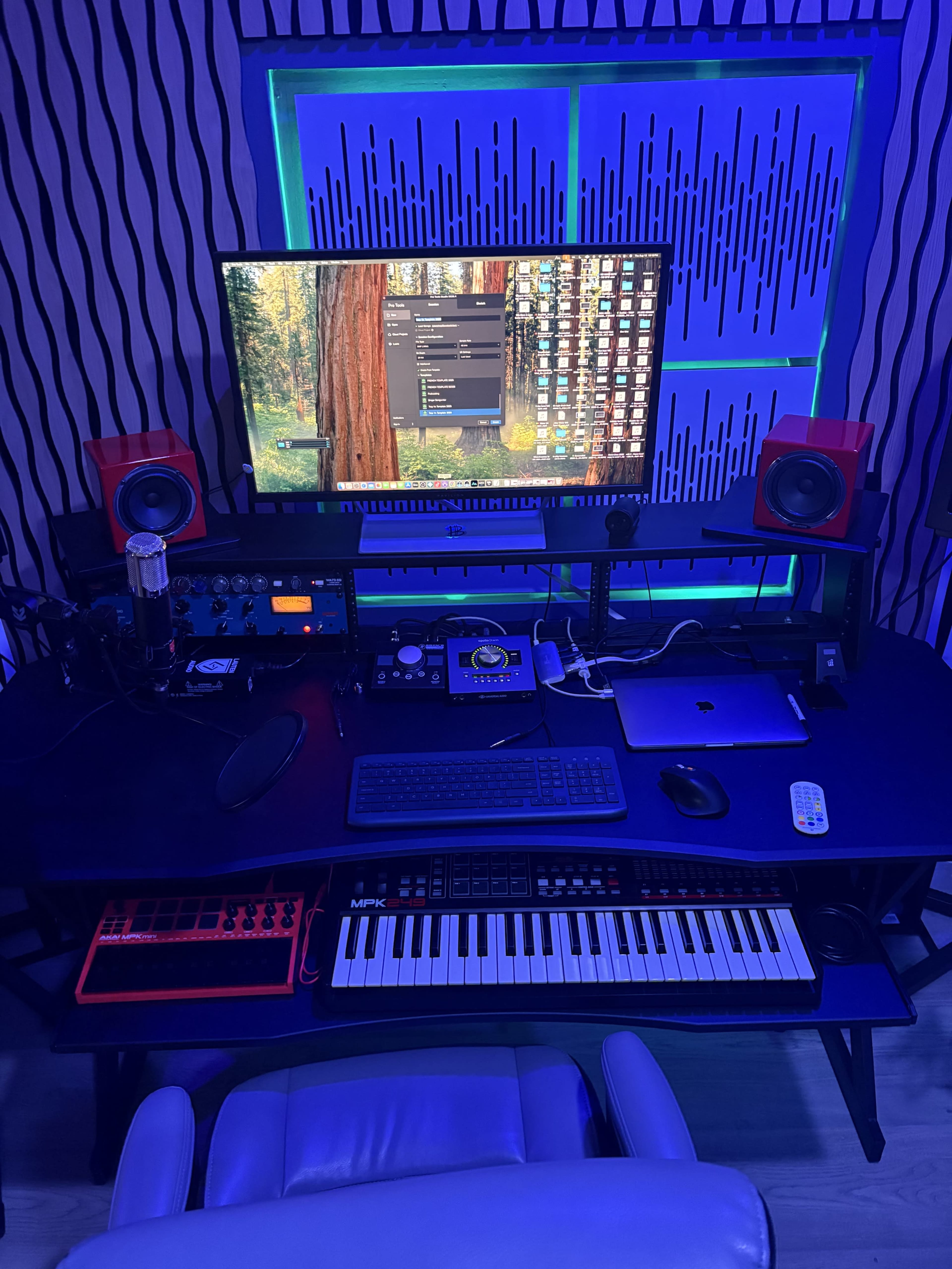 The image depicts a home recording studio with a computer monitor, audio equipment, a keyboard, and a controller set on a desk, all illuminated by blue lighting.