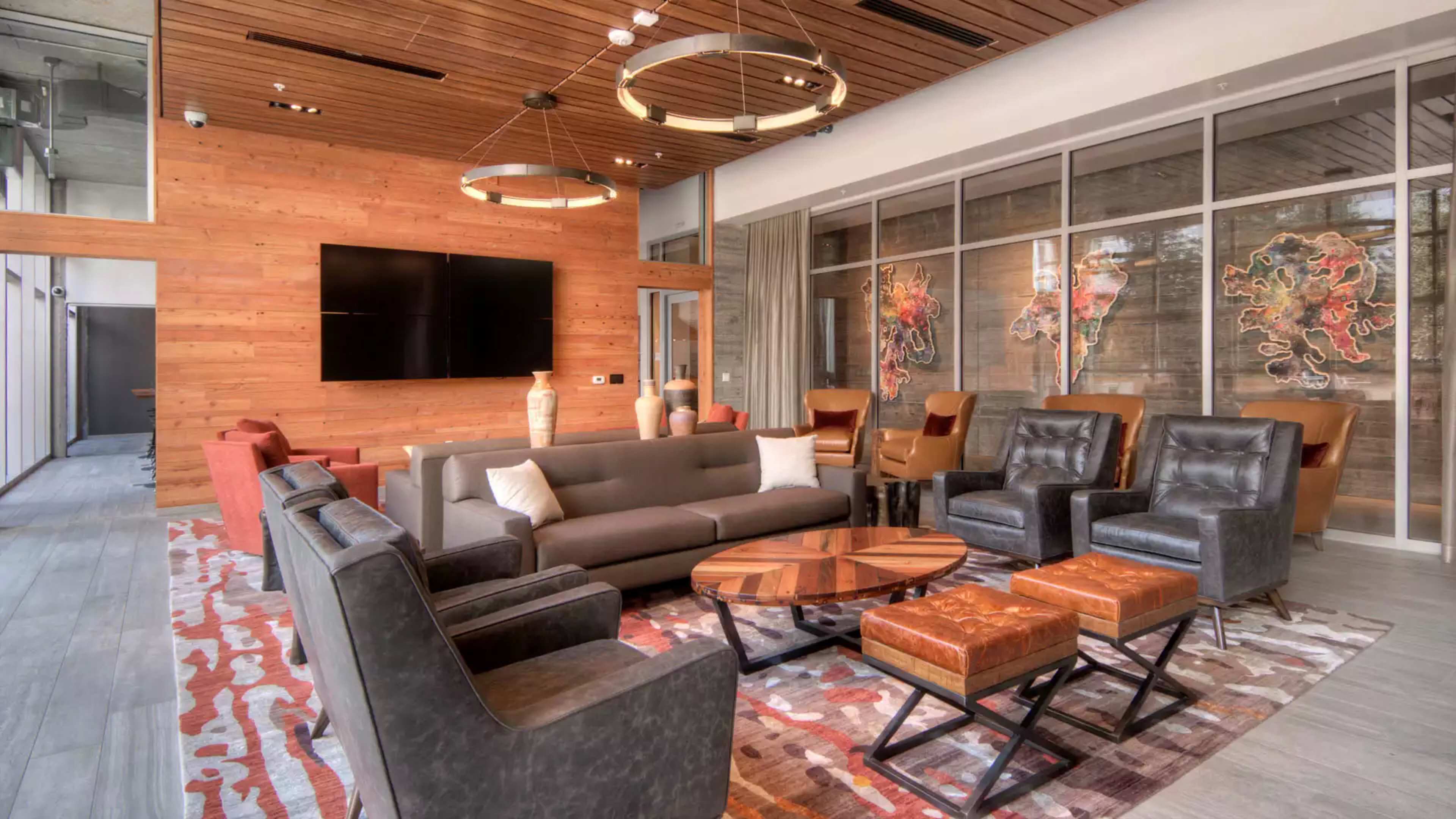 A modern lounge area featuring a sectional sofa, several armchairs, a coffee table, and a large TV mounted on a wooden wall.