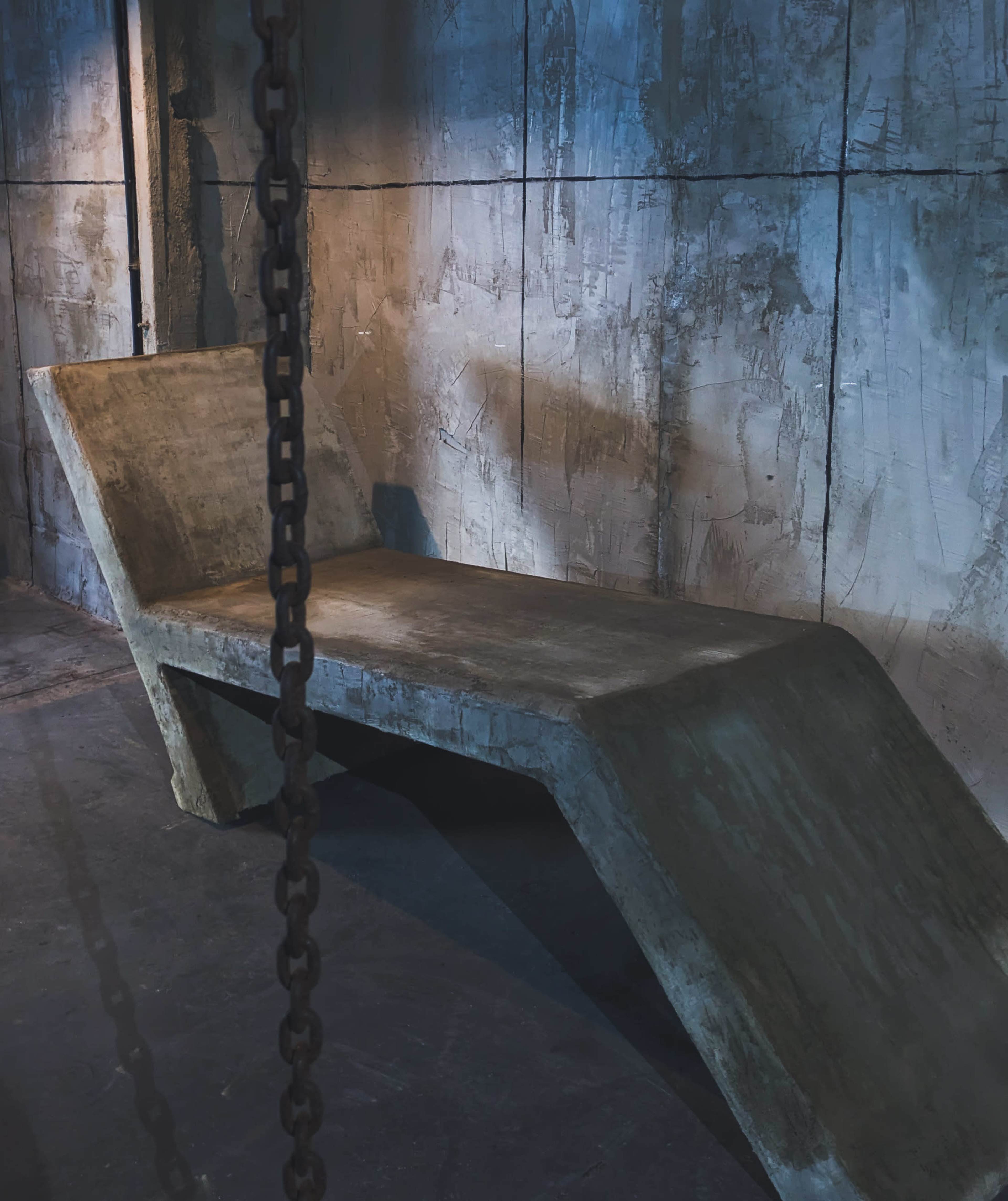 The image shows a sleek, modern concrete lounge chair against a textured wall with dramatic lighting.