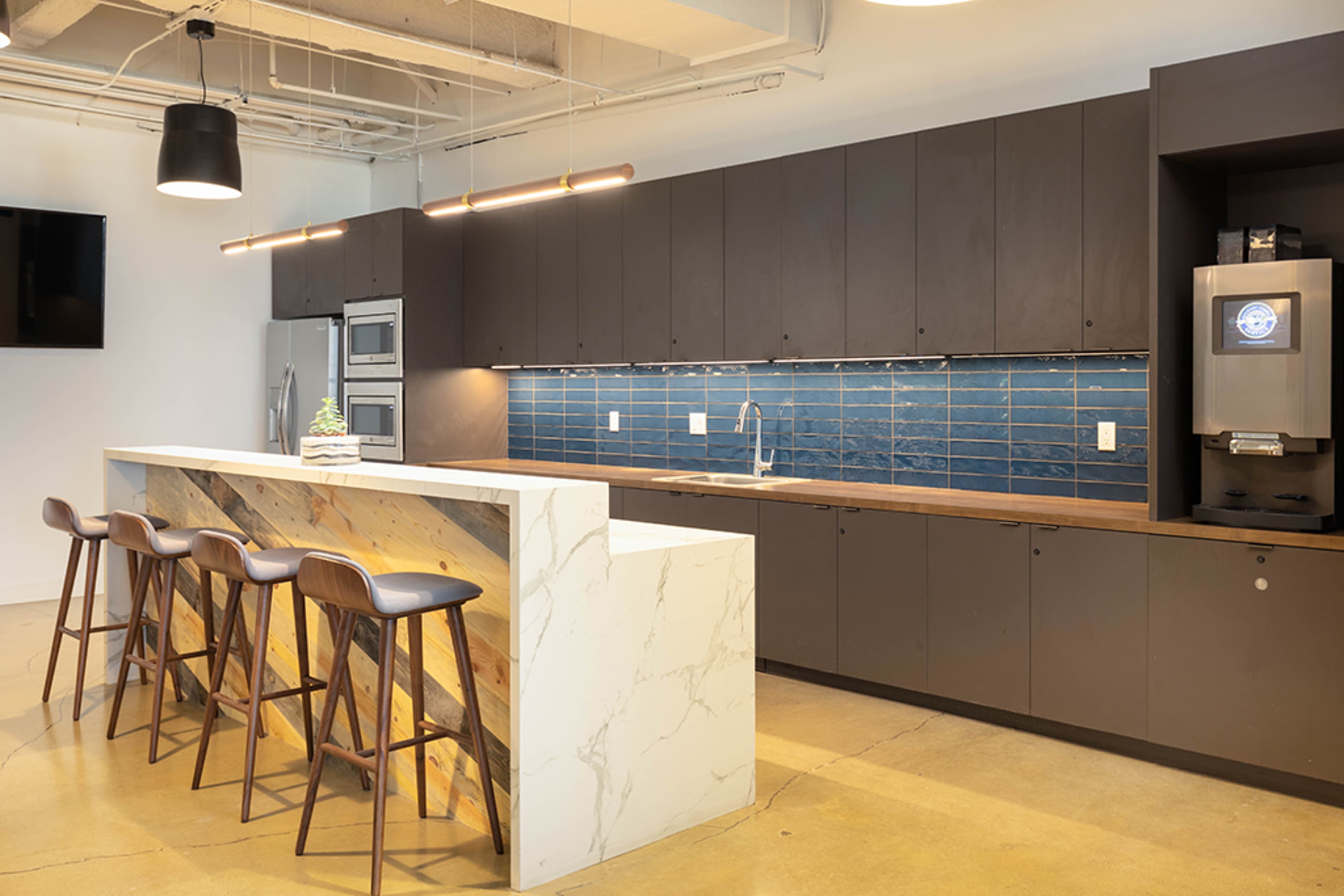 A modern kitchen with a marble-top island and dark cabinetry, featuring blue tiled backsplash and bar stools.