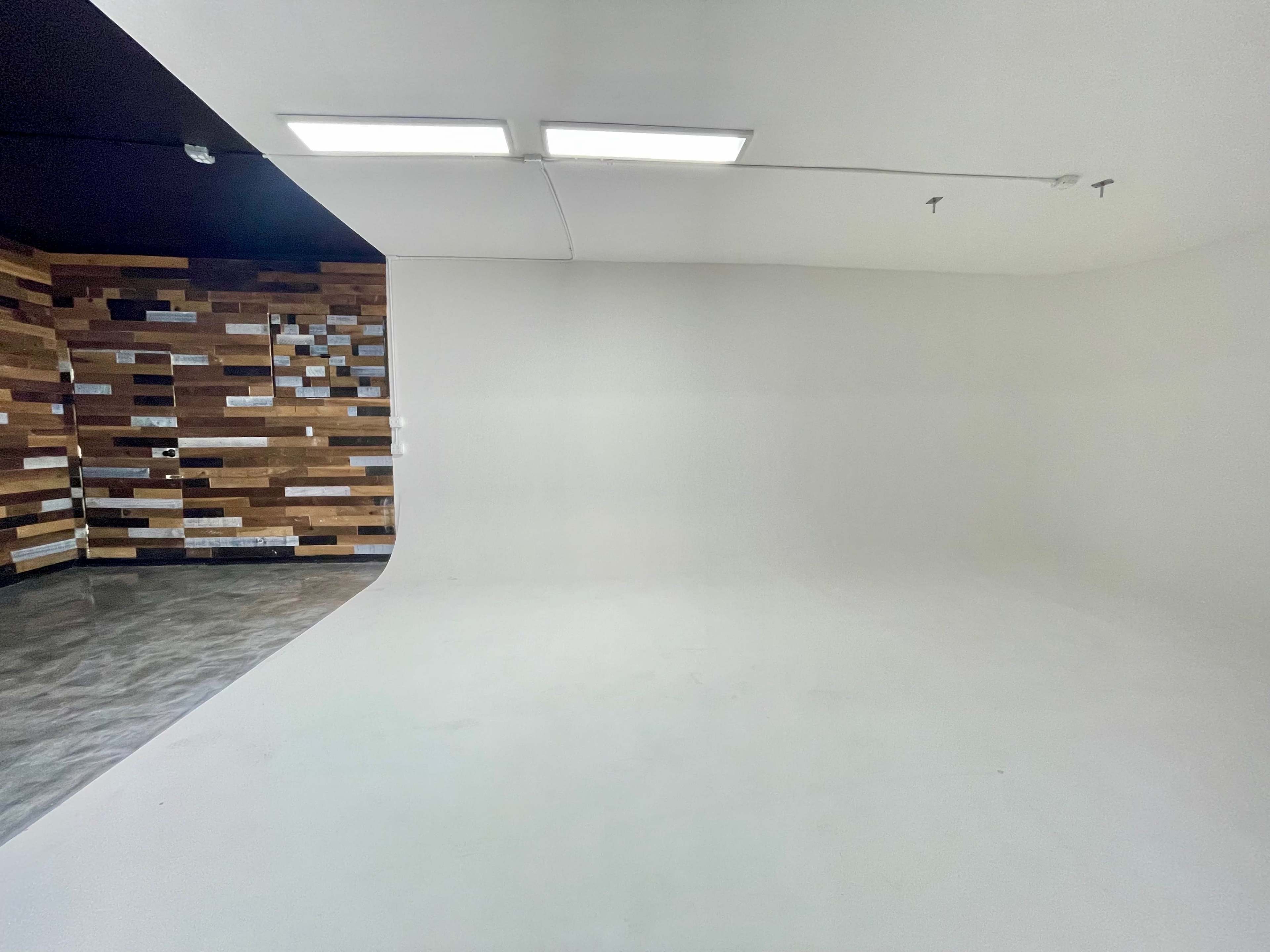 The image shows a spacious room with a white curved wall and a wooden accent wall featuring various rectangular panels.