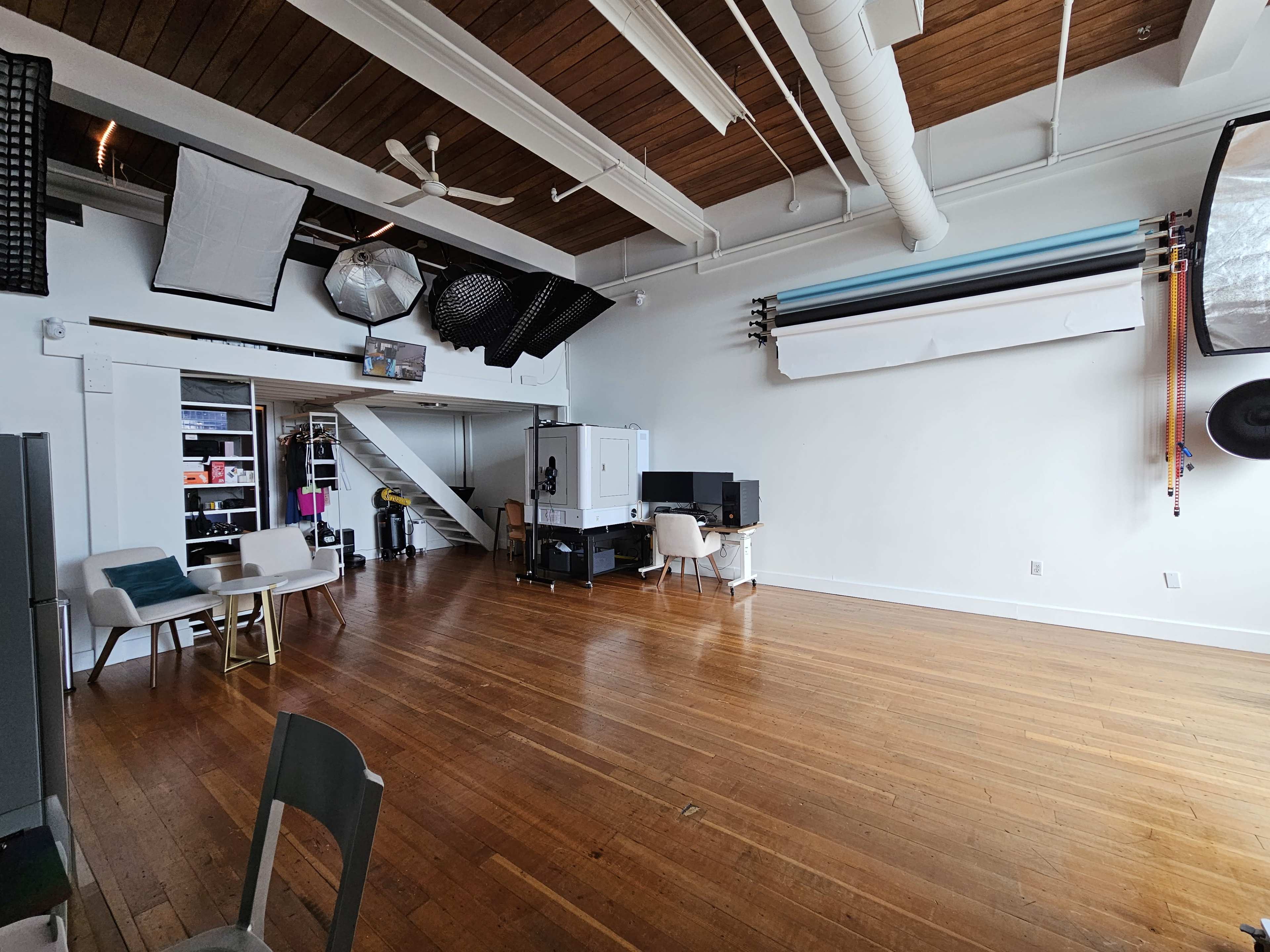 A spacious, well-lit studio with wooden floors, white walls, and various equipment stored on one side.