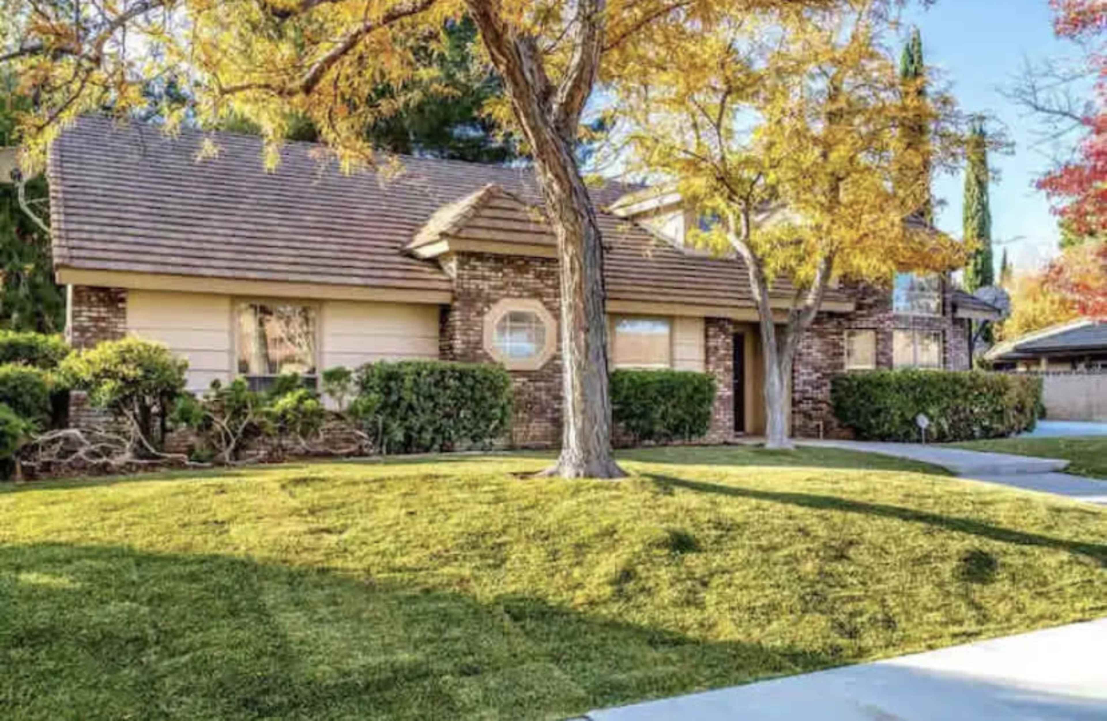 A single-story brick house with a well-maintained lawn and surrounding trees in autumn colors.