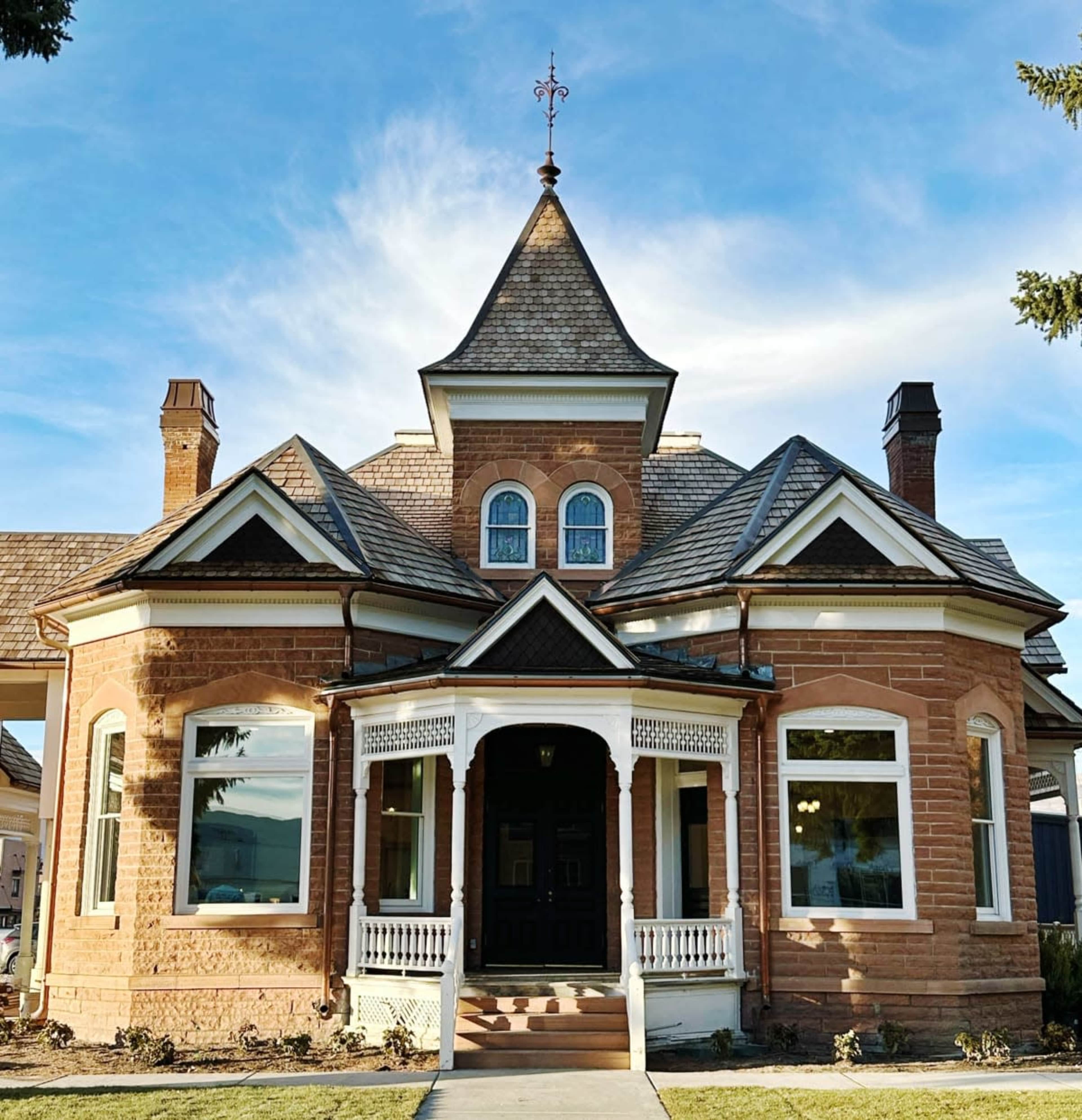 A large, historic two-story house with a steeply pitched roof, ornate architectural details, and a welcoming front porch.