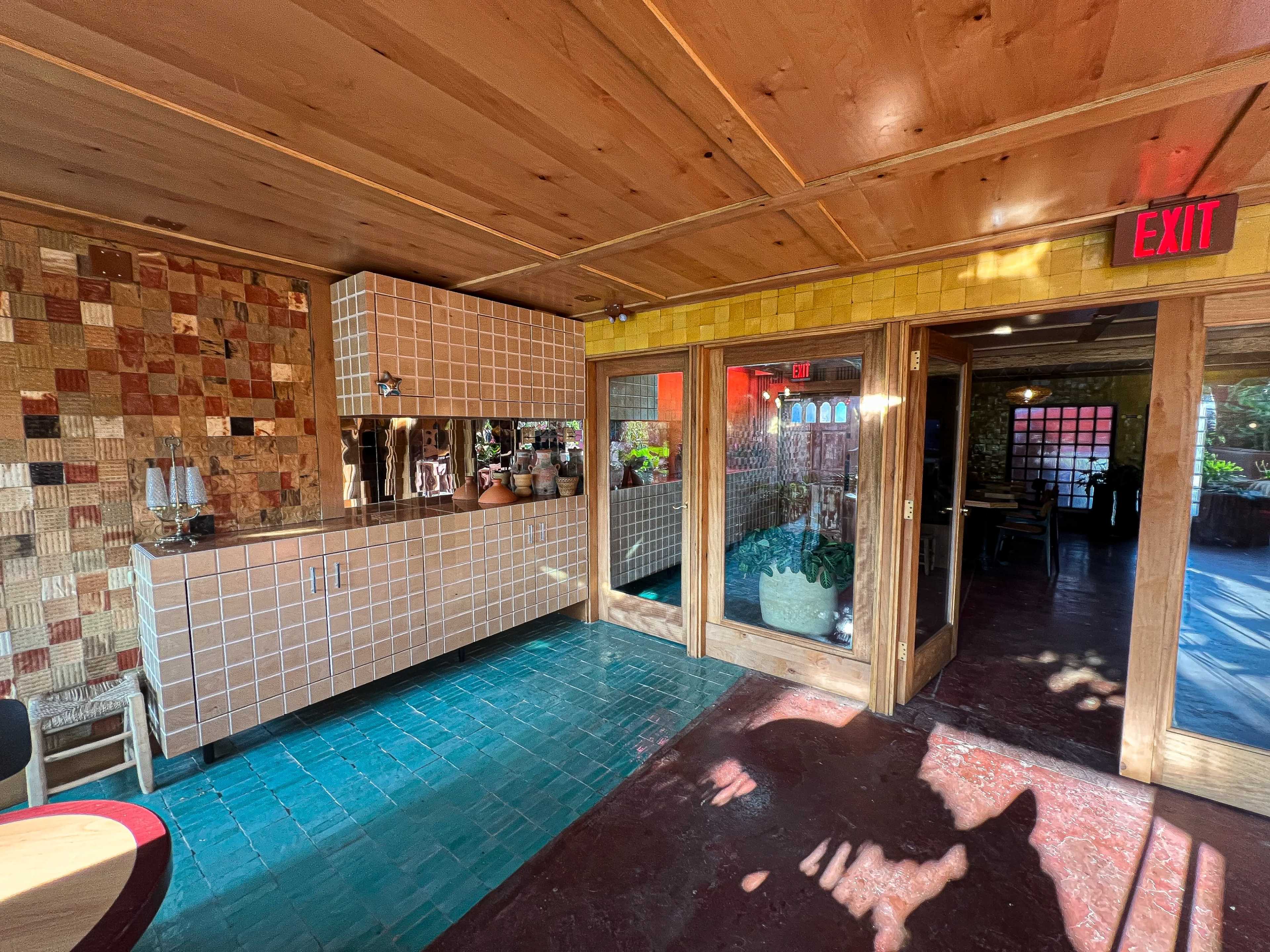 The interior of a restaurant features tiled walls, a wooden ceiling, and glass doors leading outside.