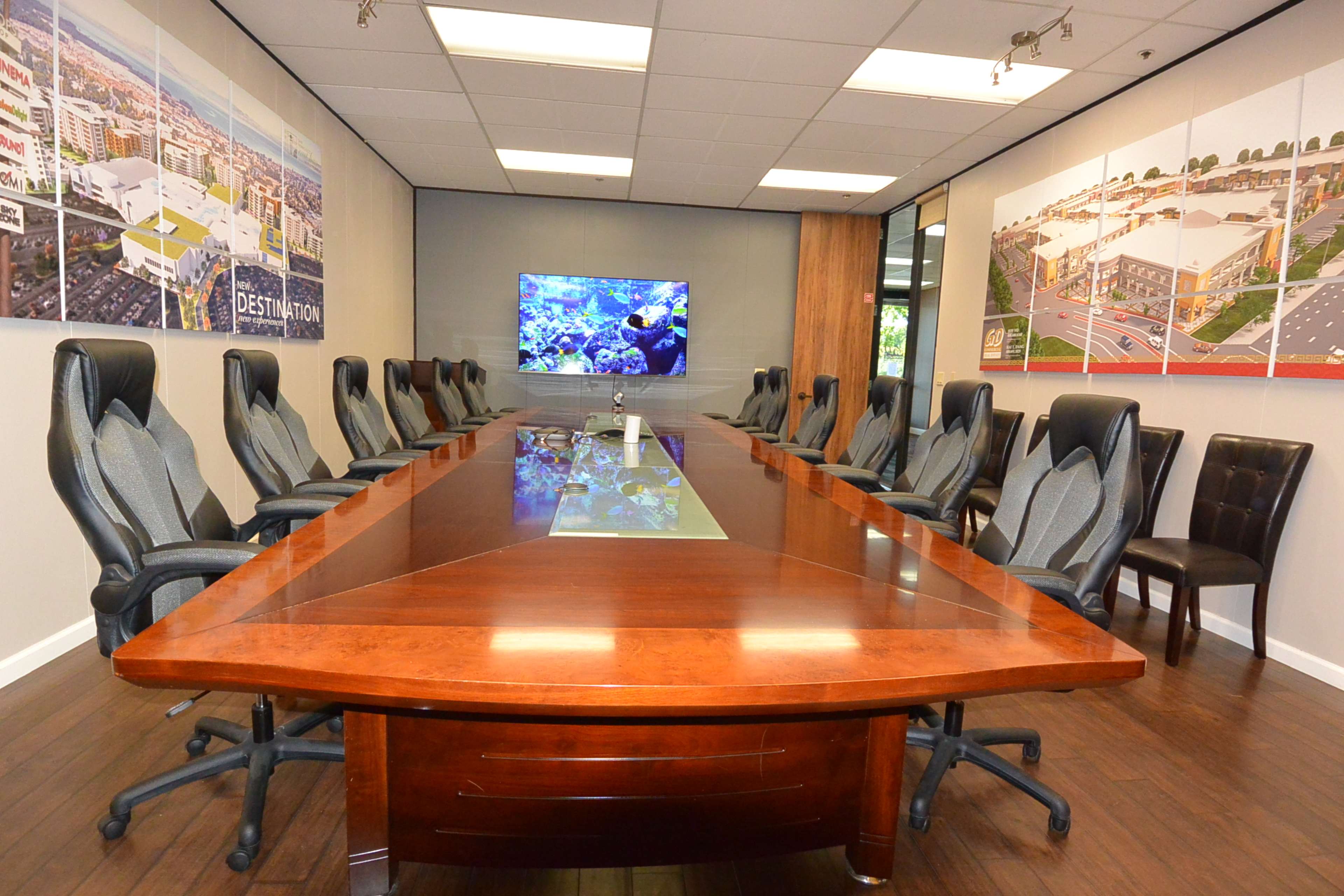 A conference room with a large wooden table surrounded by high-backed chairs, and a television mounted on the wall displaying an underwater scene.