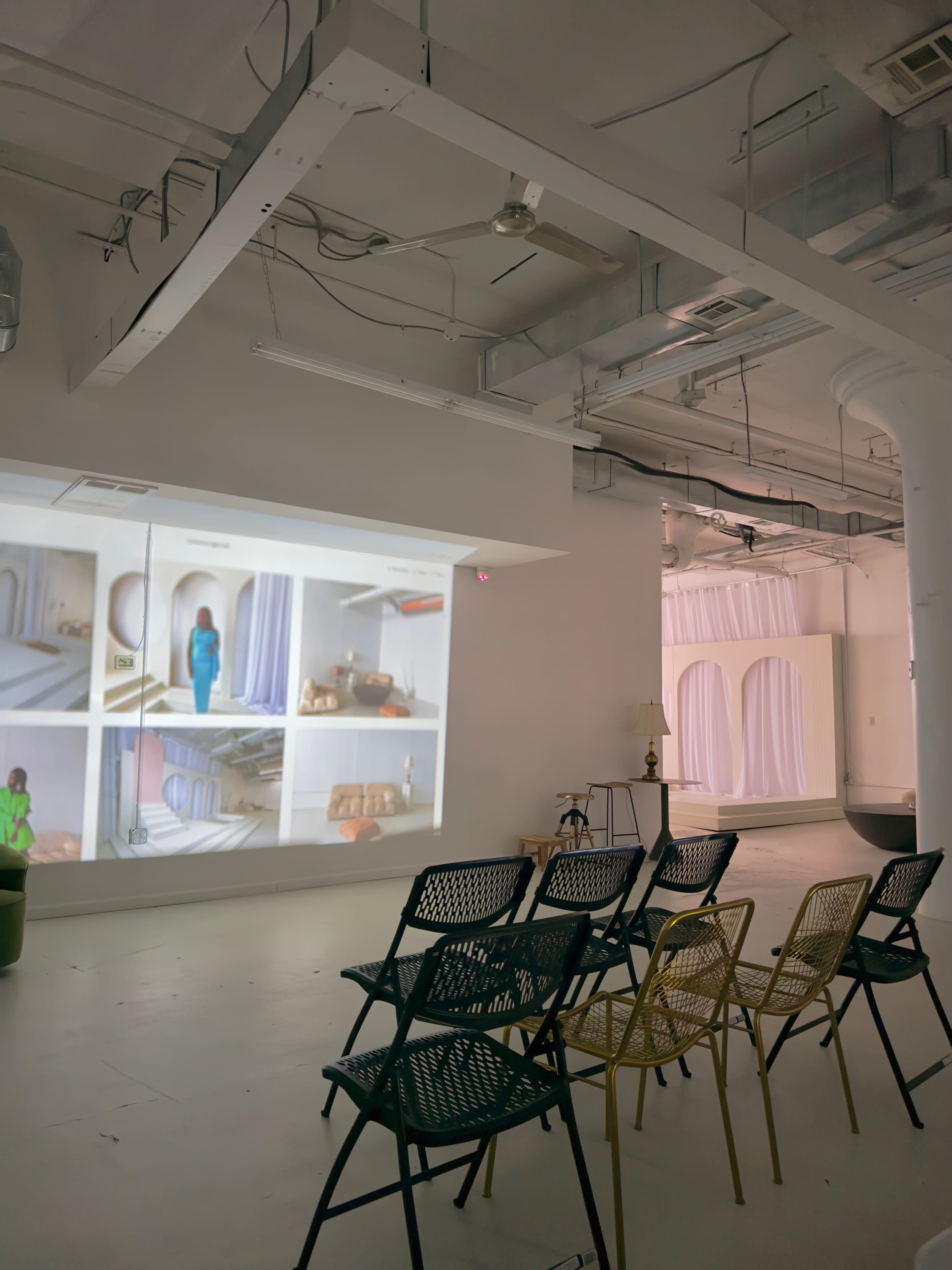 A spacious gallery with a wall projection displaying various interior designs, accompanied by a row of chairs arranged for seating.