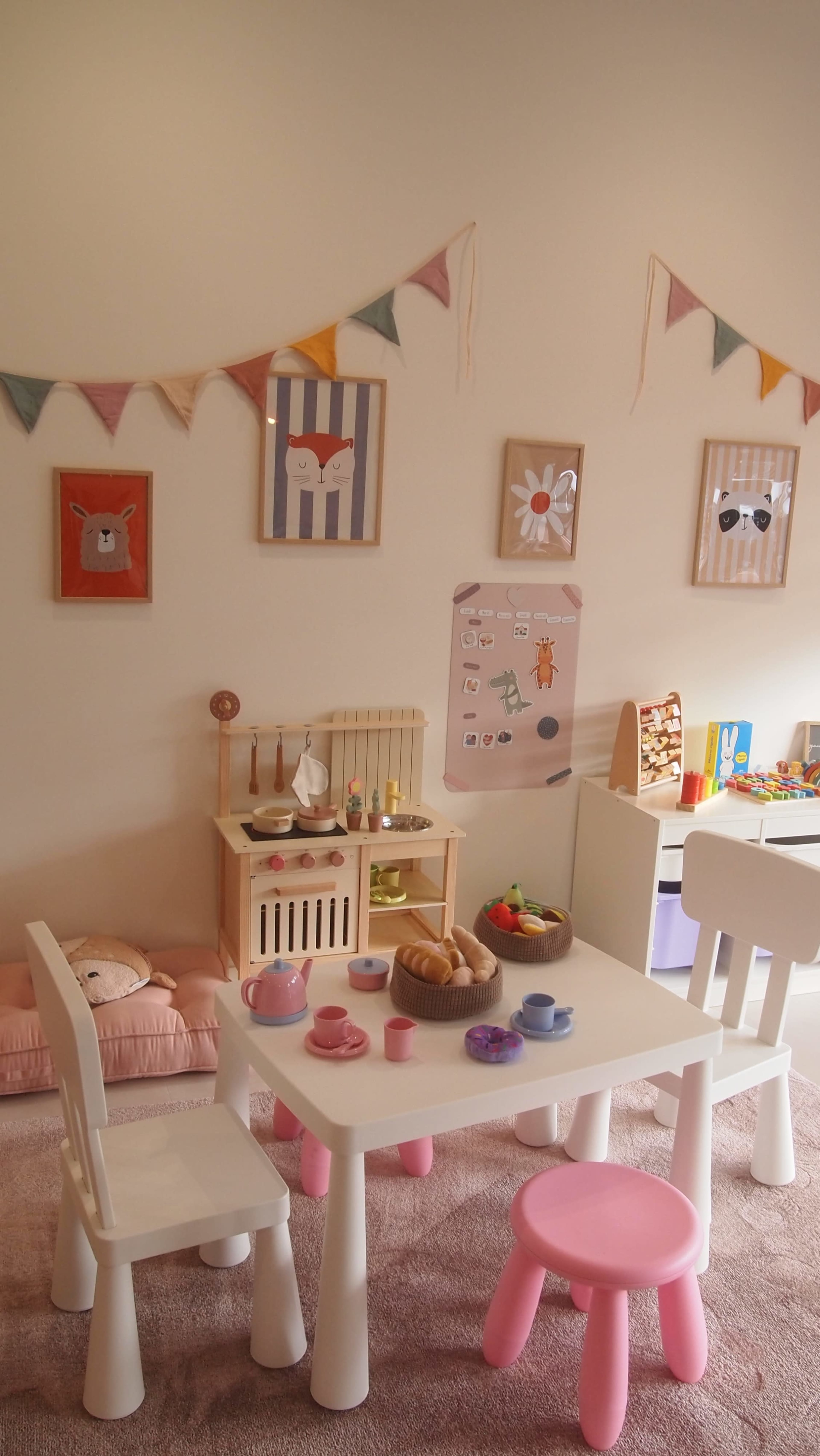 A playroom is decorated with cheerful wall art, a small table set with mini food items, and a cozy seating area with a soft cushion.