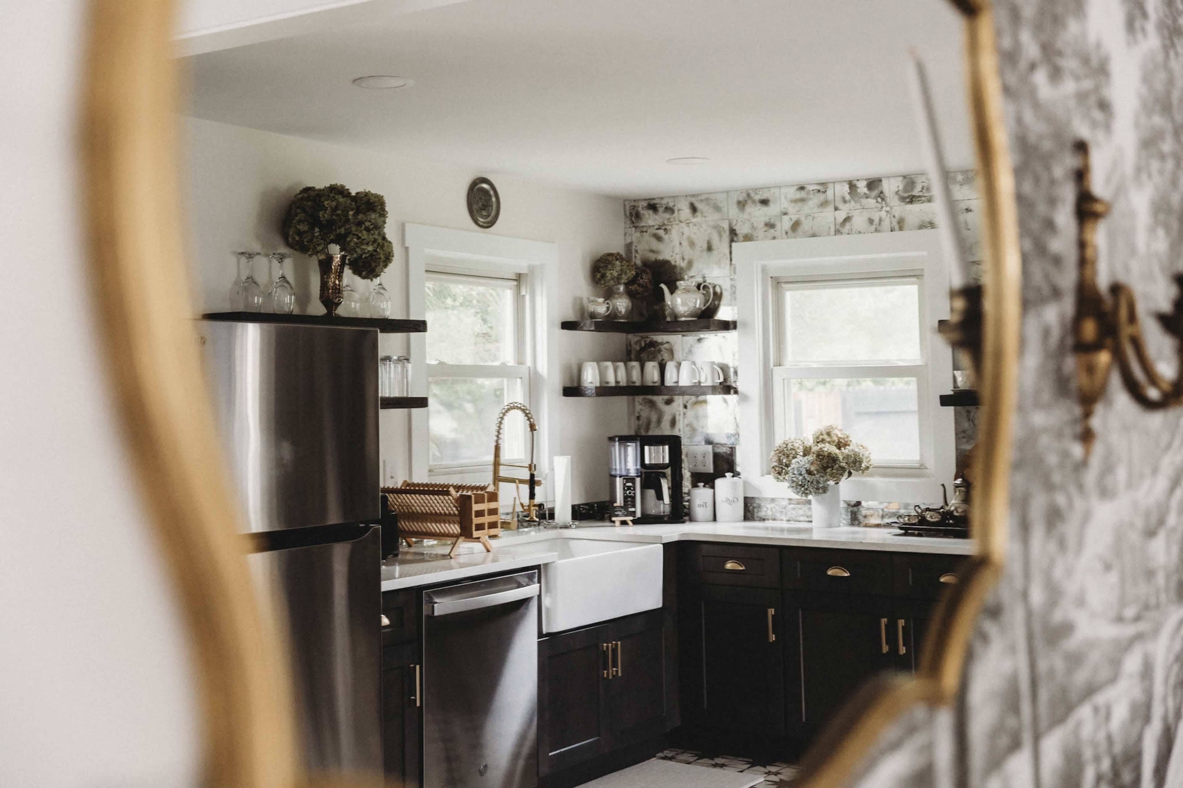 A spacious kitchen features dark cabinets, a farmhouse sink, and shelves adorned with glassware and decorative items.