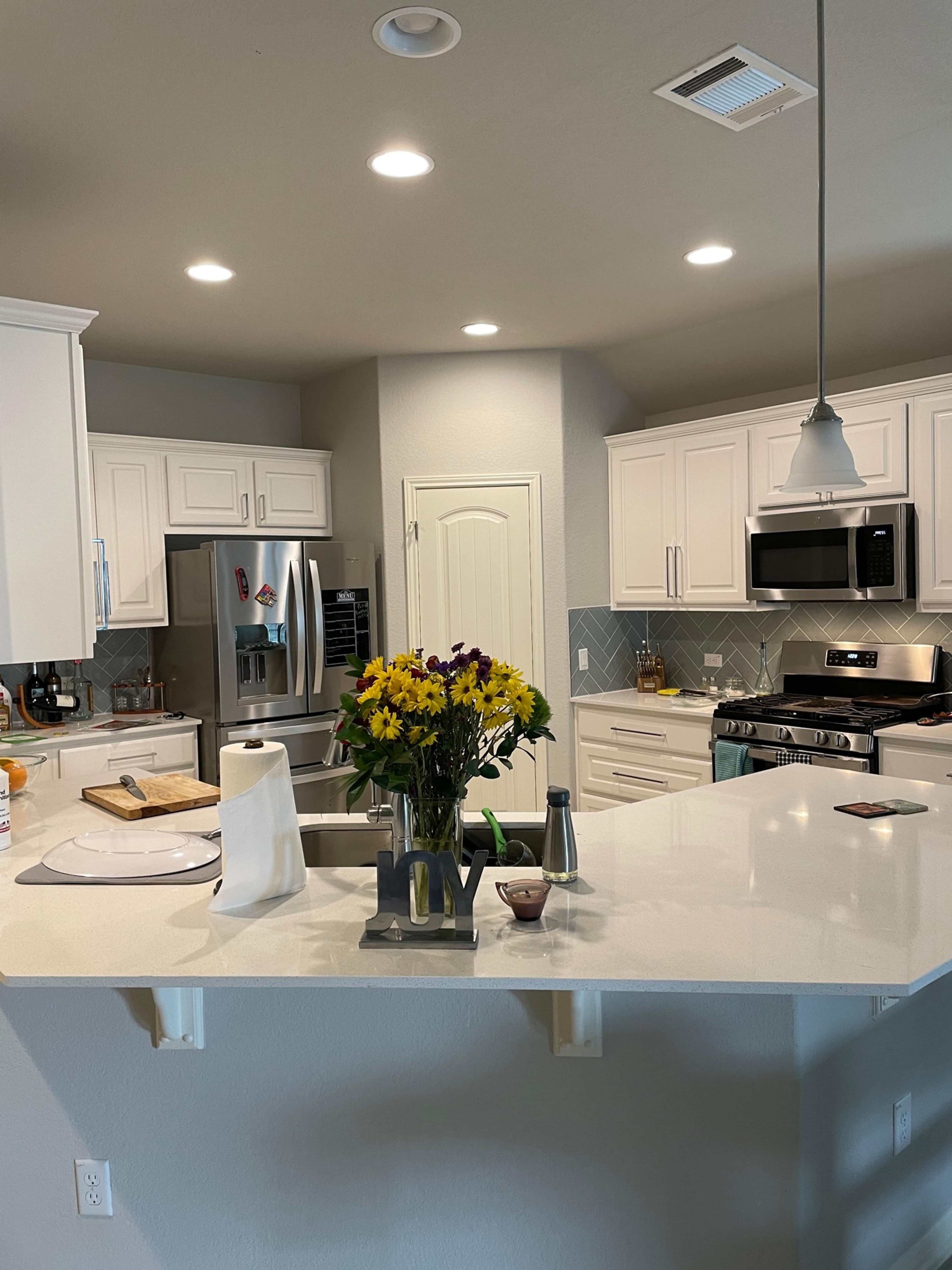 A modern kitchen features white cabinets, stainless steel appliances, and a center island with a bouquet of flowers.