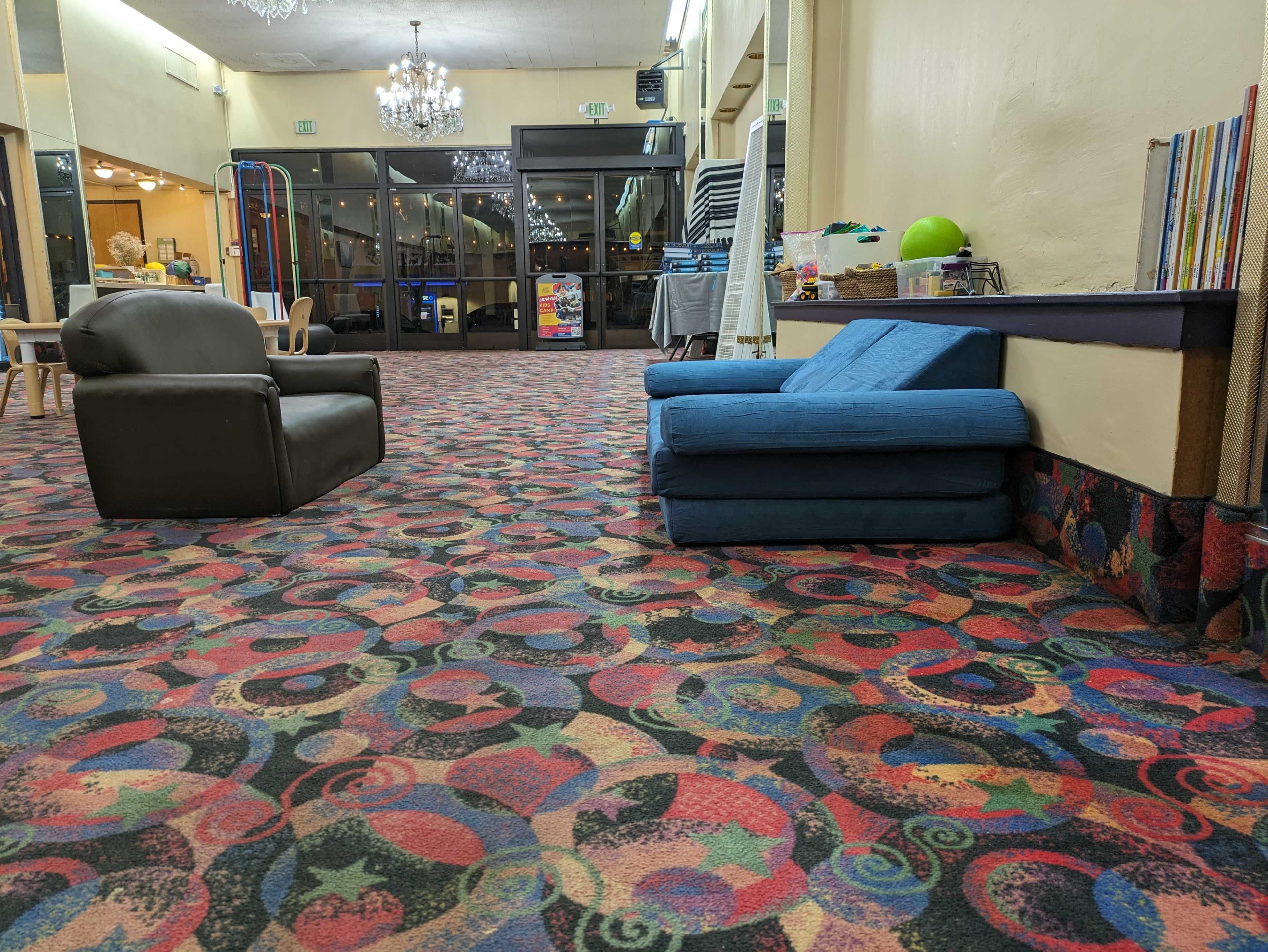 A lounge area with a black armchair and a blue sofa against a patterned carpet, while the space is illuminated by overhead lights.