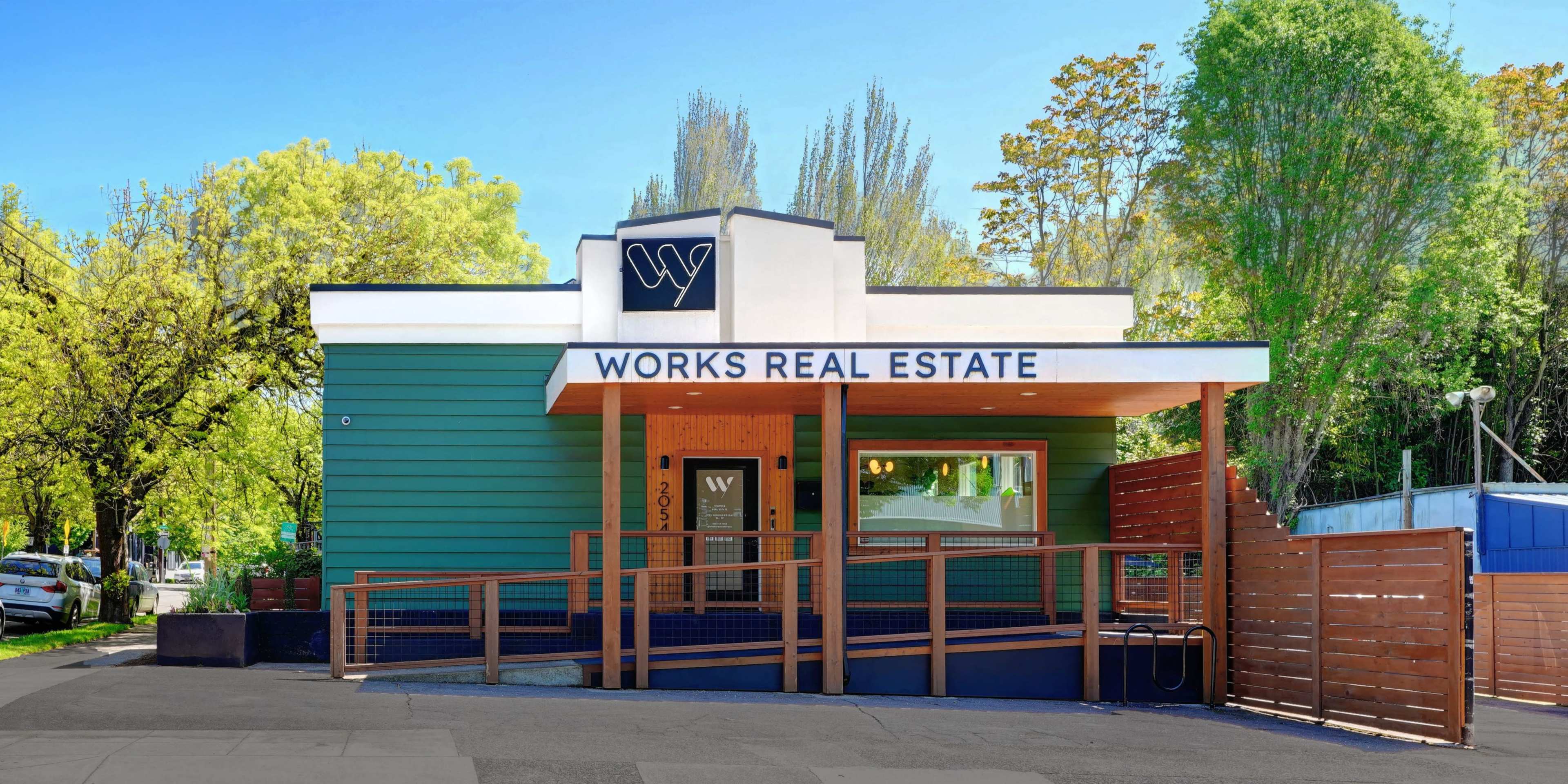 The image shows a two-story building with a green exterior and a prominent sign that reads "WORKS REAL ESTATE" at the entrance.