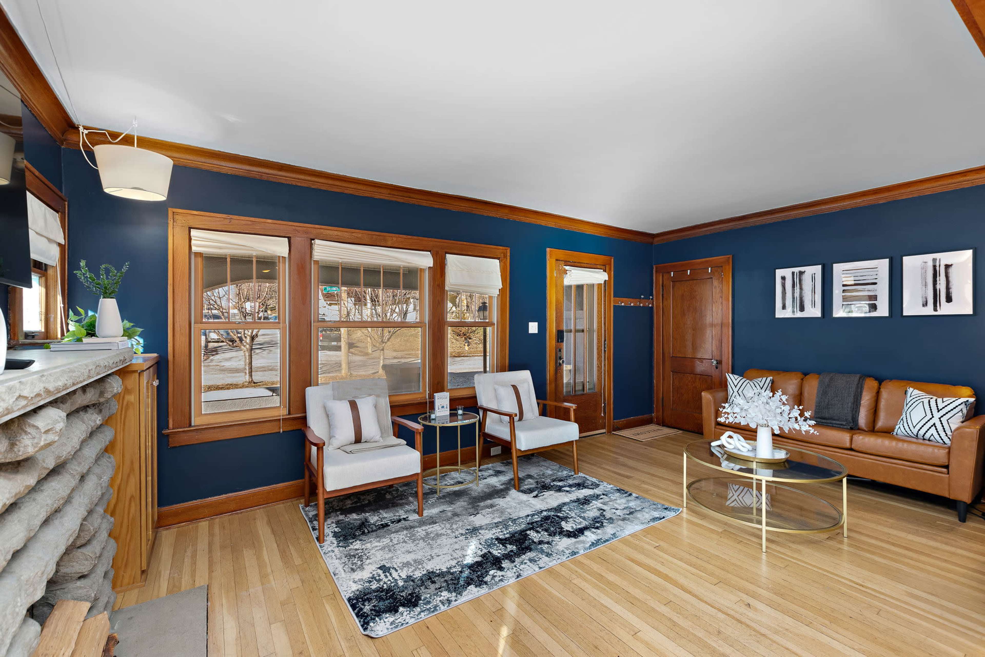 A living room with a brown leather sofa, two upholstered chairs, a glass coffee table, and large windows that provide natural light.