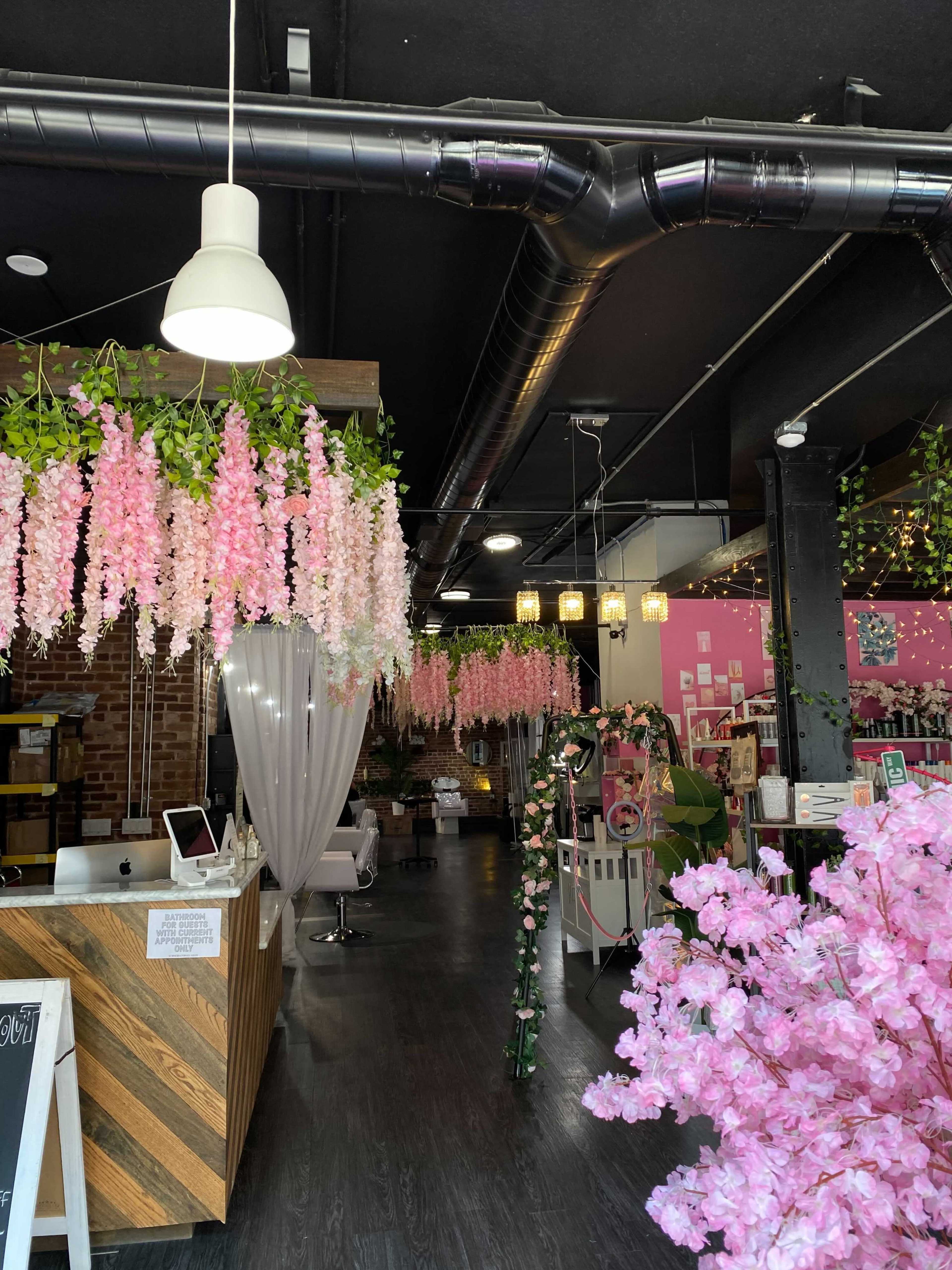 A modern floral shop interior with hanging pink and white decorations, a reception area, and various floral arrangements.