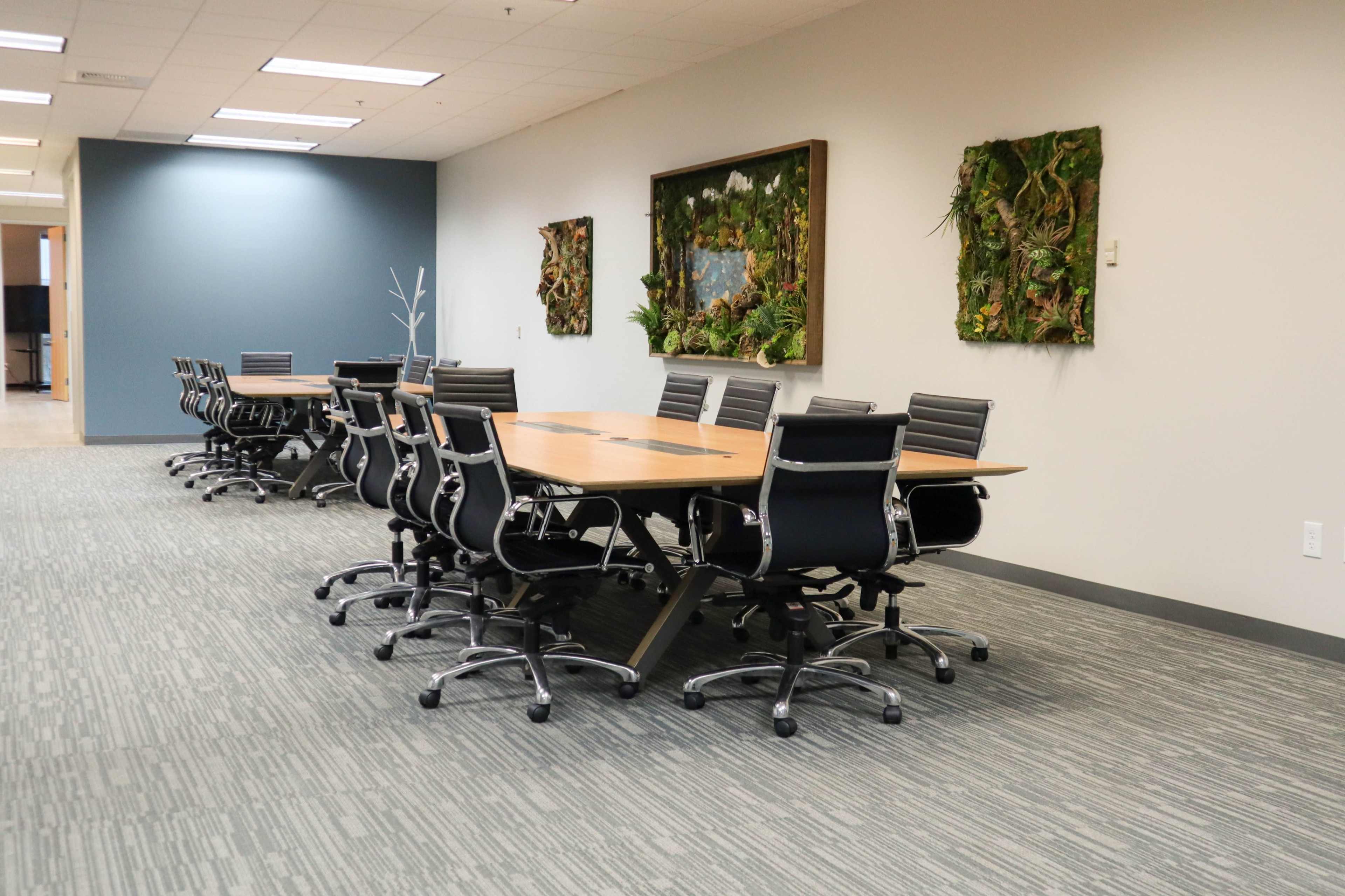 A spacious conference room features a long wooden table surrounded by black chairs and decorated with two vertical garden panels on the walls.