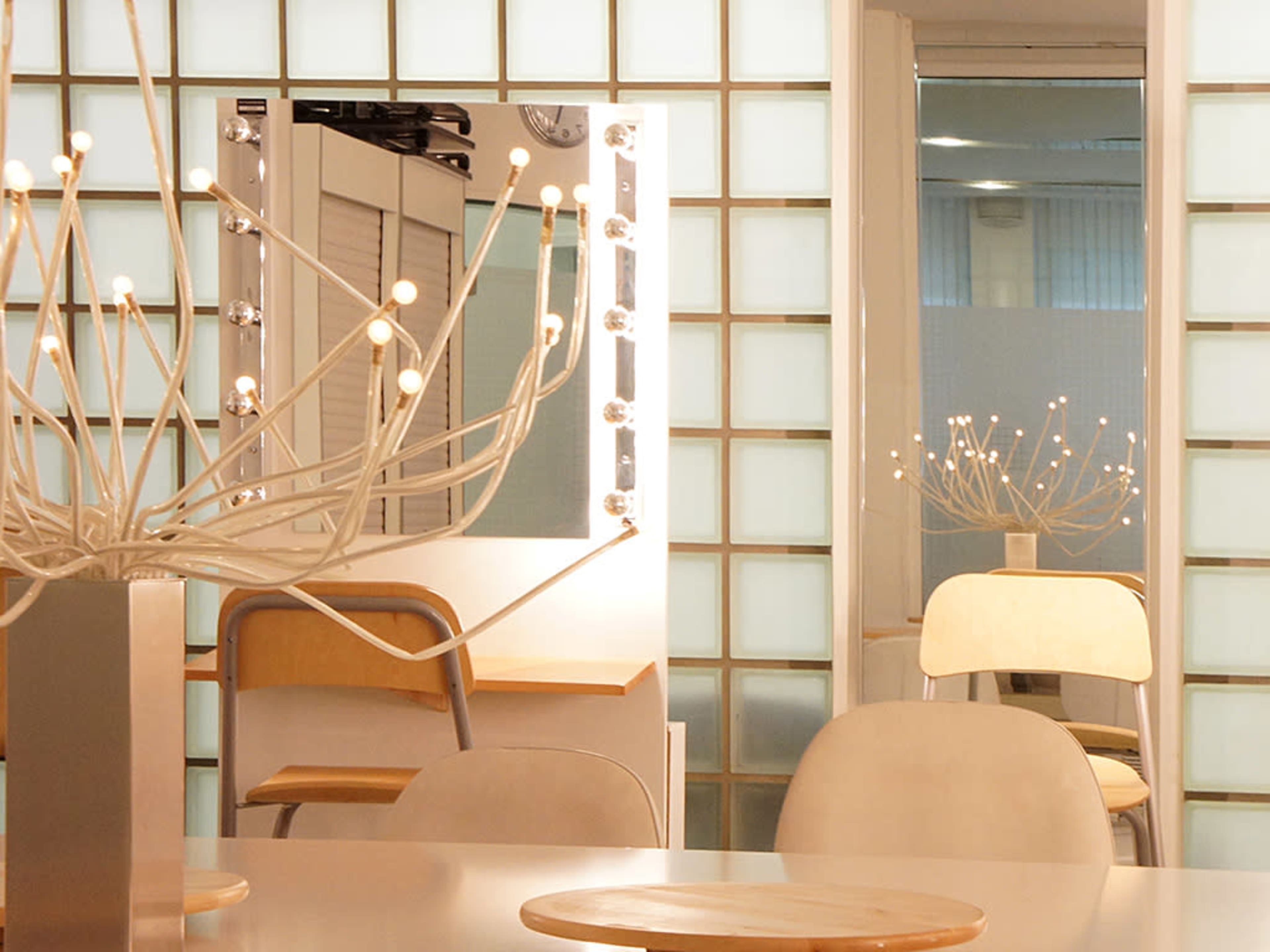 A modern dressing room with a lighted mirror, a minimalist chair, and glass block walls.