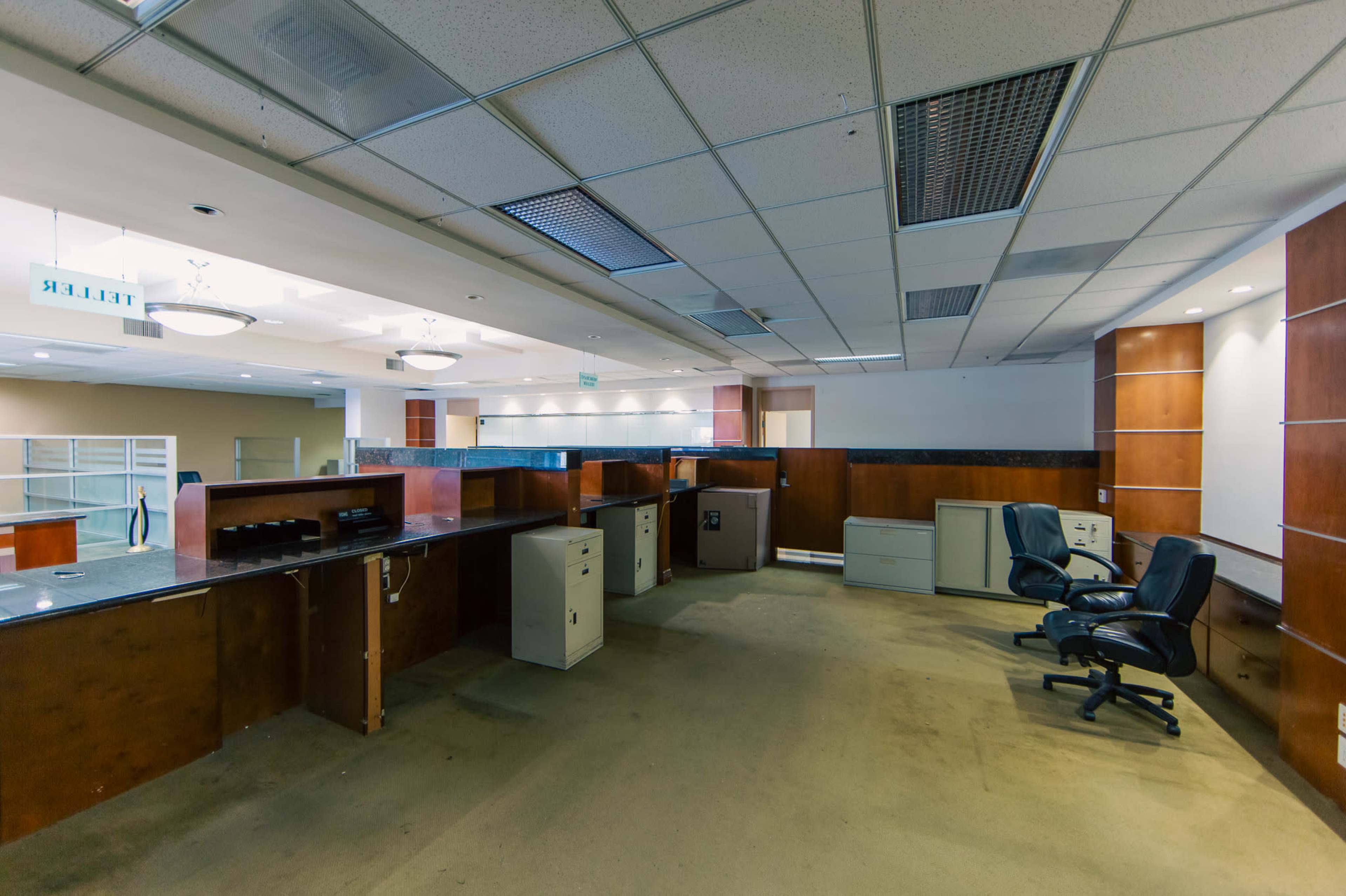 The image depicts a spacious office area with several empty desks, filing cabinets, and two office chairs.