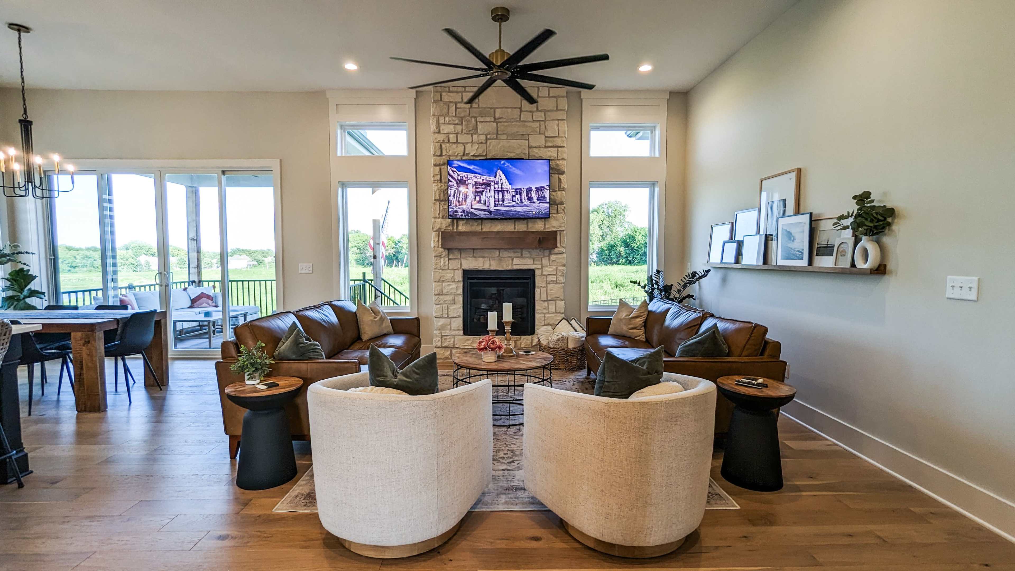 A modern living room featuring a stone fireplace with a television above it, complemented by two leather sofas and two armchairs arranged around a coffee table.