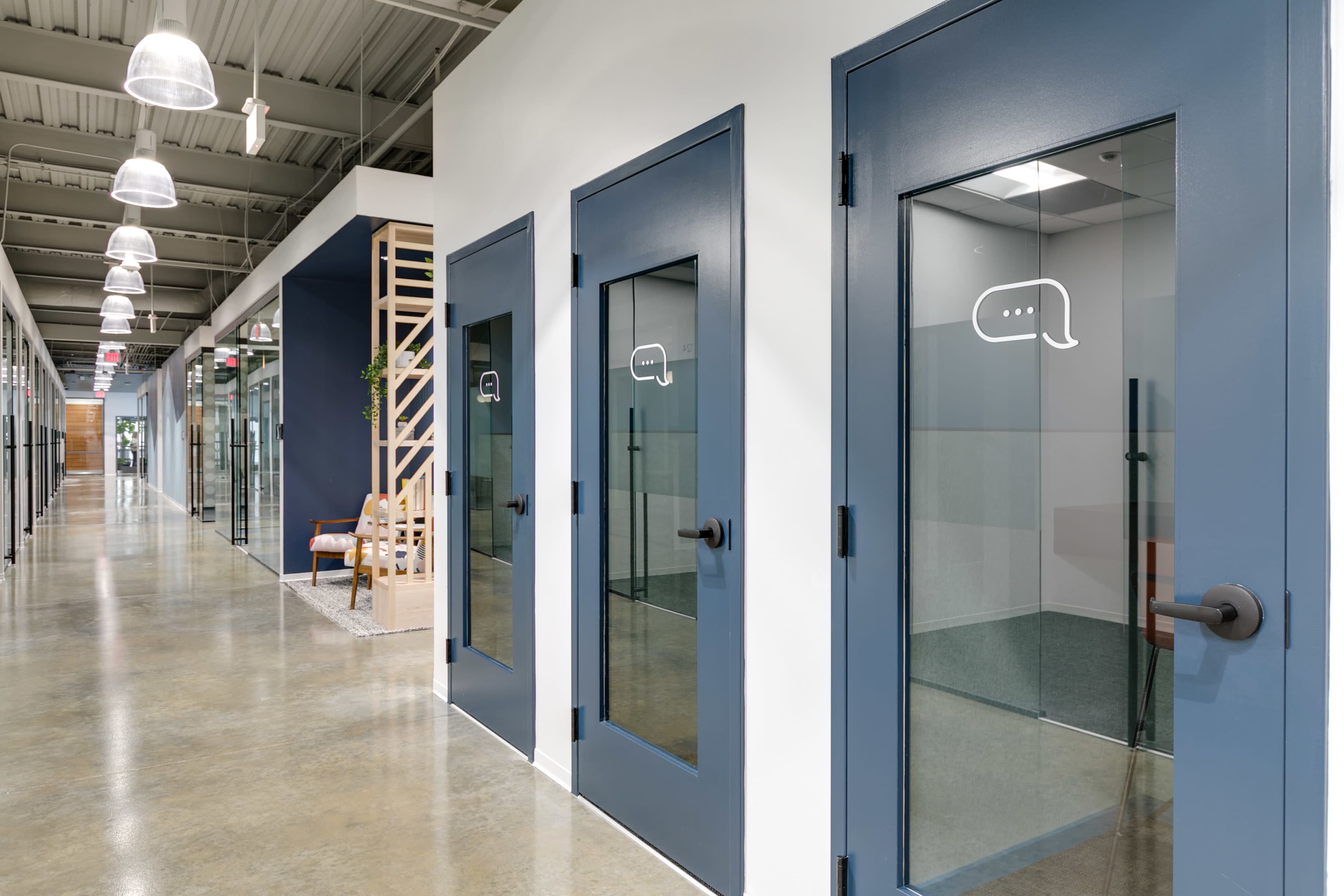 A modern office hallway with several glass-walled meeting rooms and a minimalist design.
