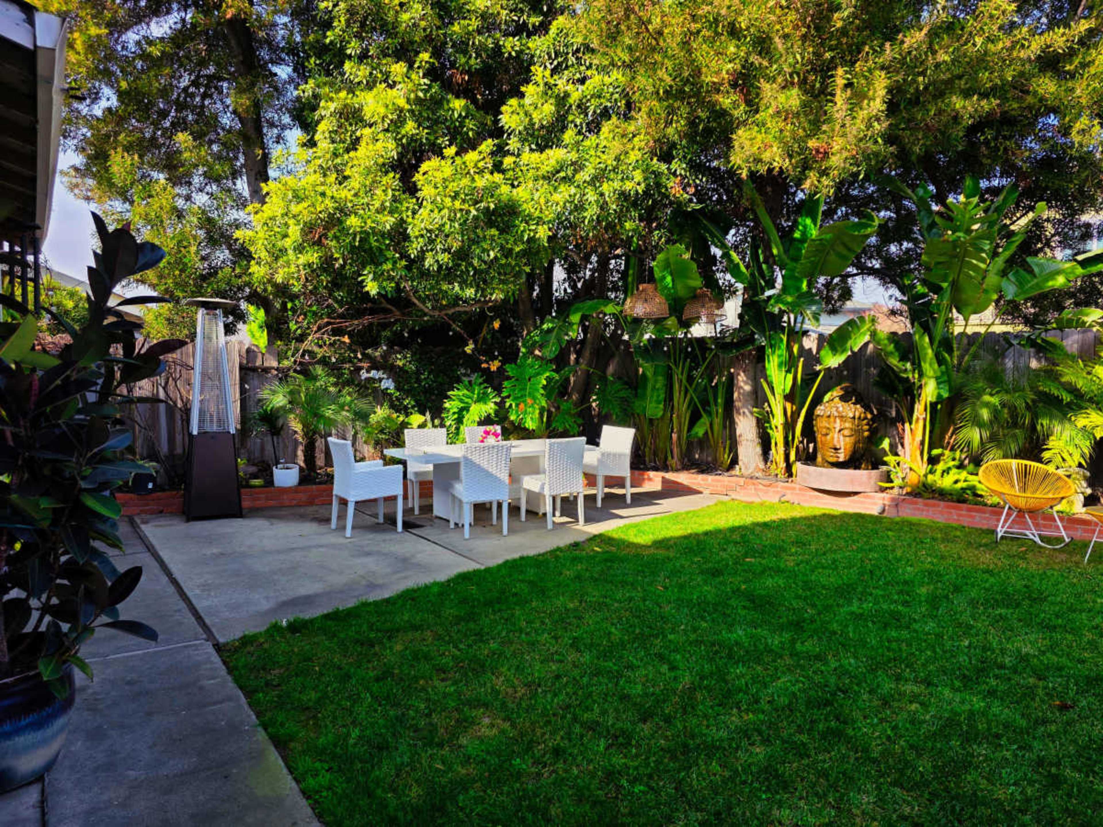 A patio area features a dining set surrounded by lush greenery and decorative elements.