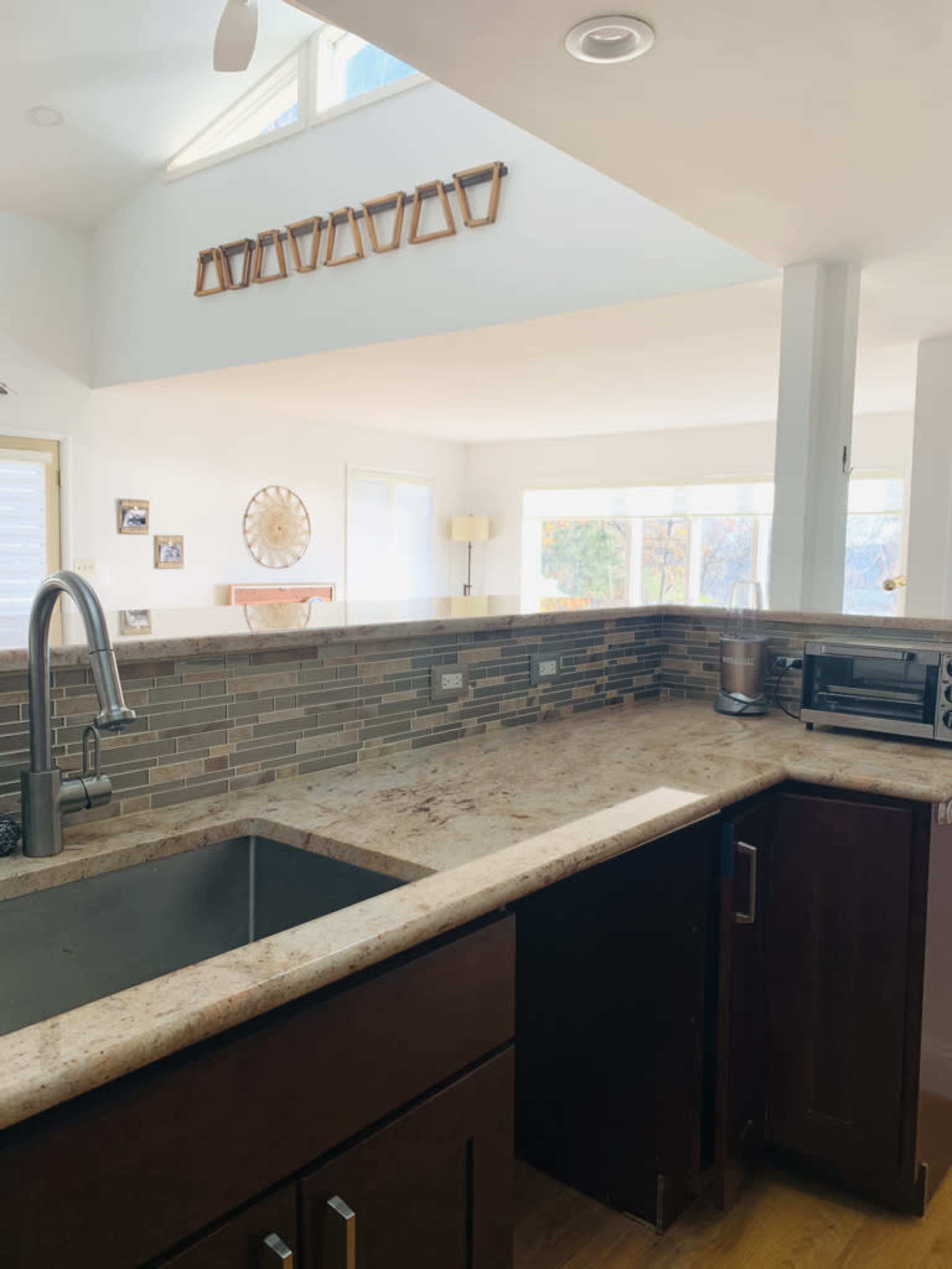 A modern kitchen features a large sink with a granite countertop, a tiled backsplash, and ample natural light from large windows.