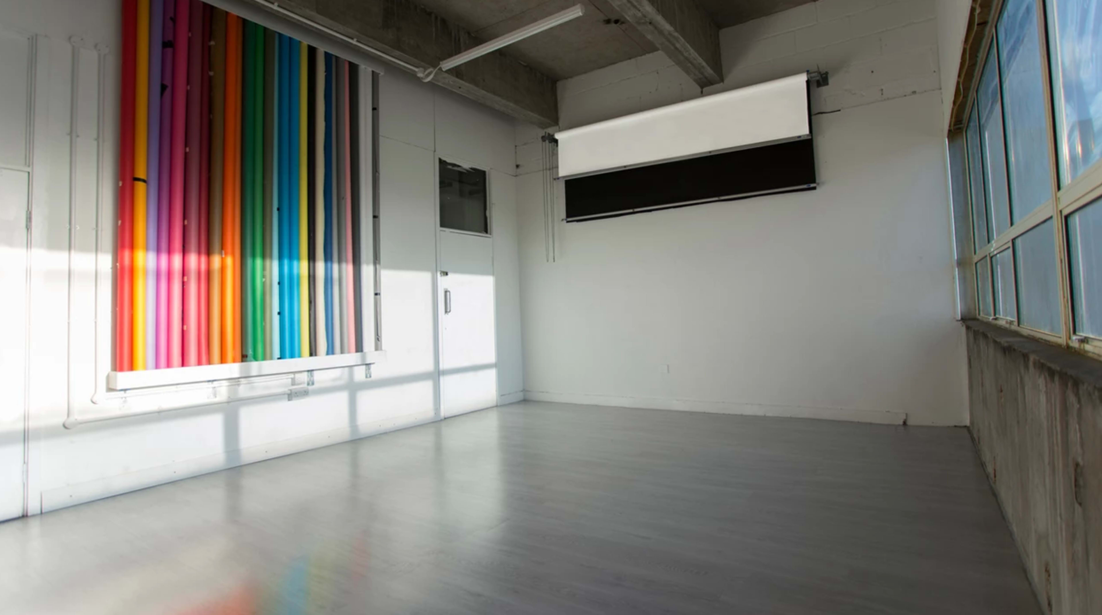 A spacious, empty room with a wall featuring colorful vertical stripes and a projector screen mounted on the ceiling.