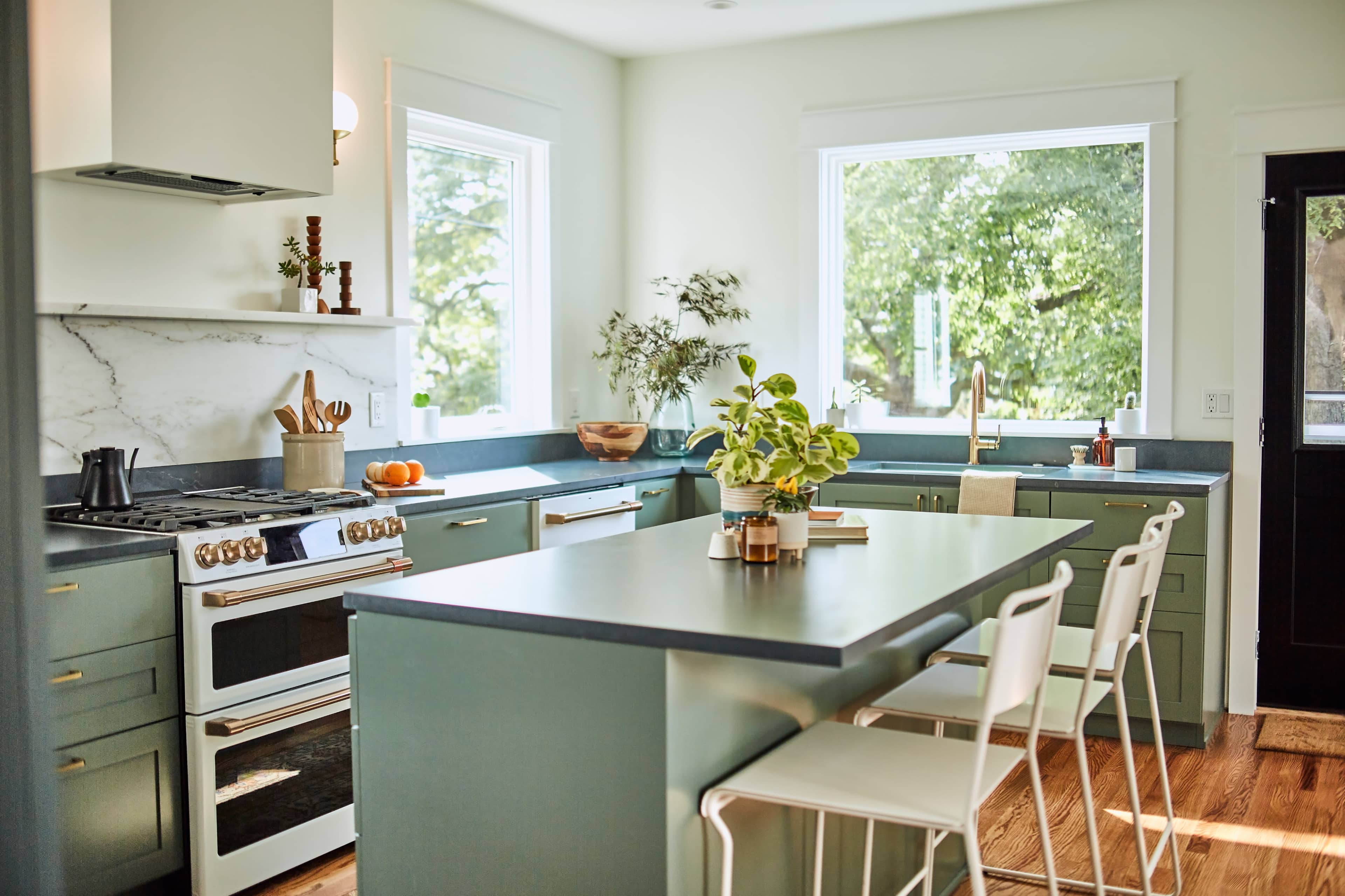 A modern kitchen features a large island with bar stools, stainless steel appliances, and ample natural light from windows overlooking greenery.