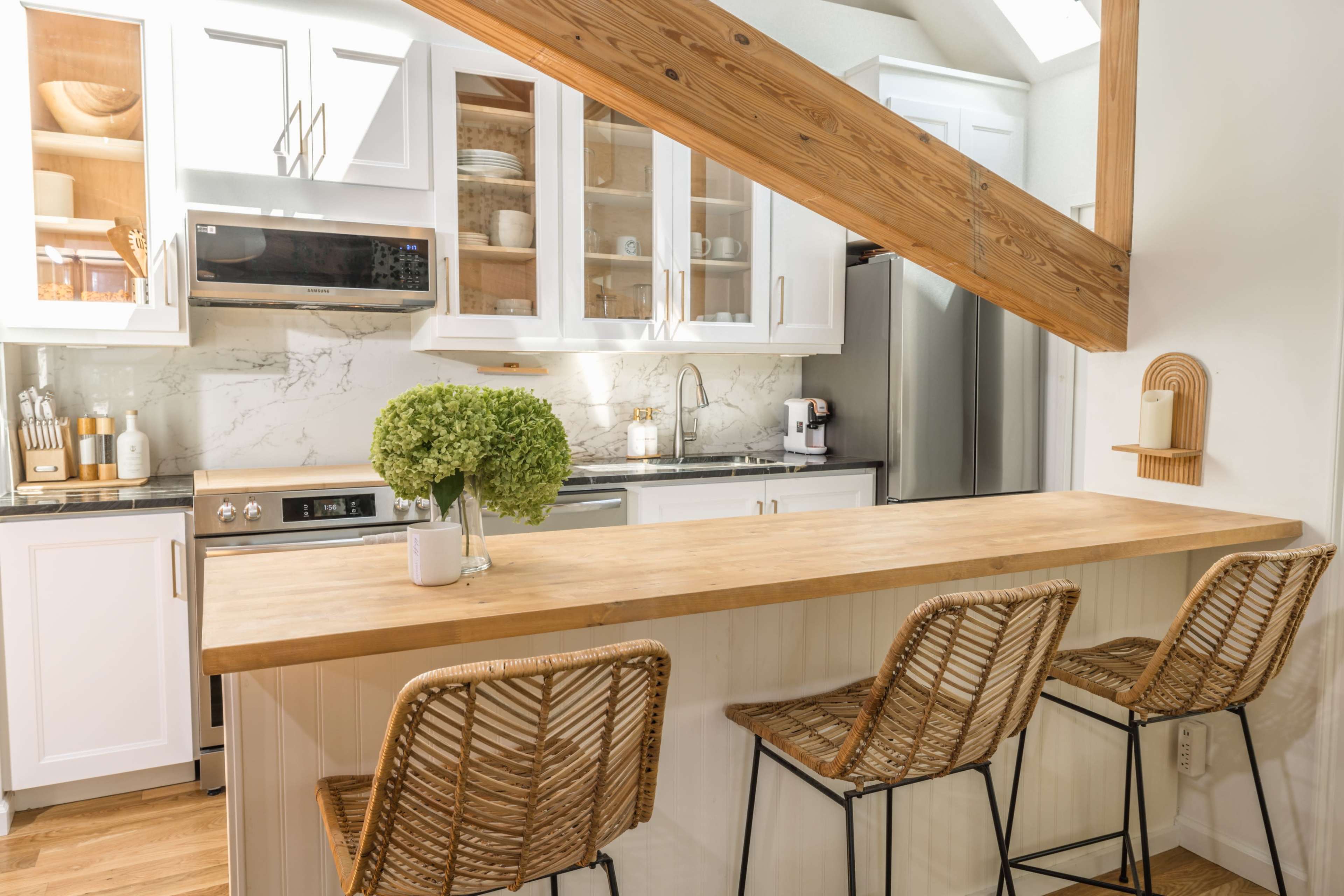 A modern kitchen features white cabinetry, a light wooden countertop, and three woven bar stools at a breakfast bar.