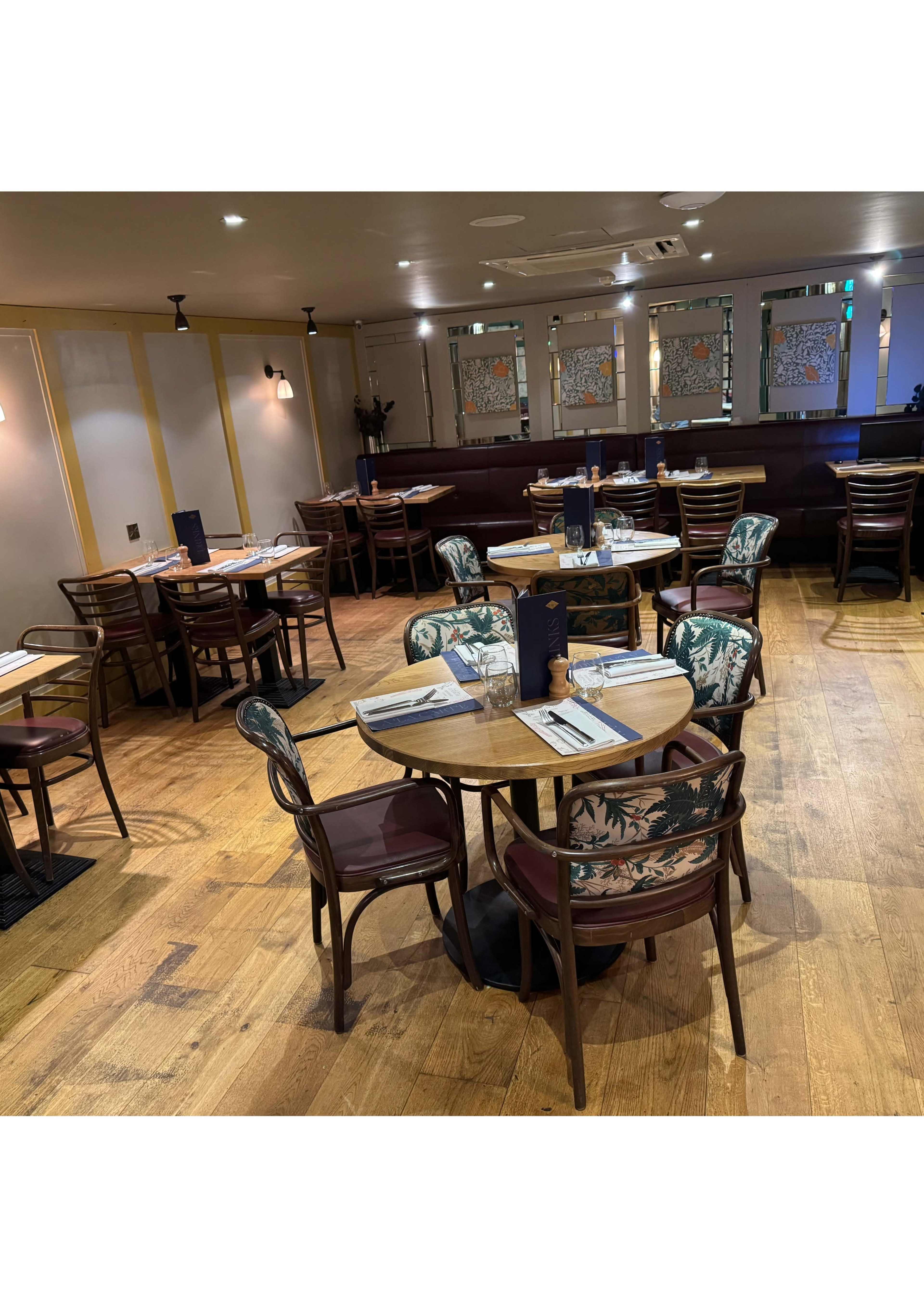 The image shows a restaurant interior with neatly arranged tables and chairs, featuring wood flooring and decorative windows.