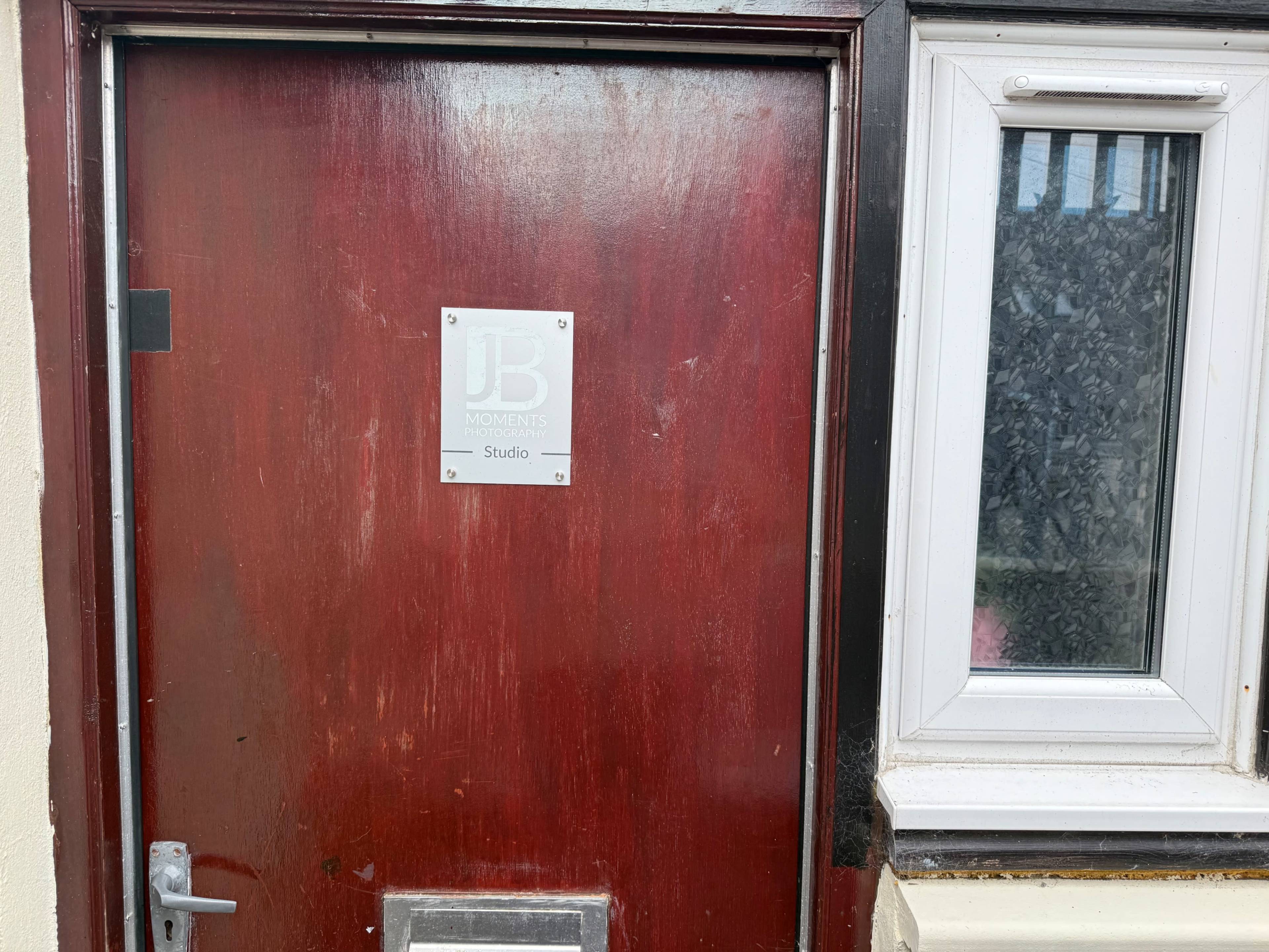 A wooden door with a metal sign labeled "JB Moments Studio" is situated next to a window.