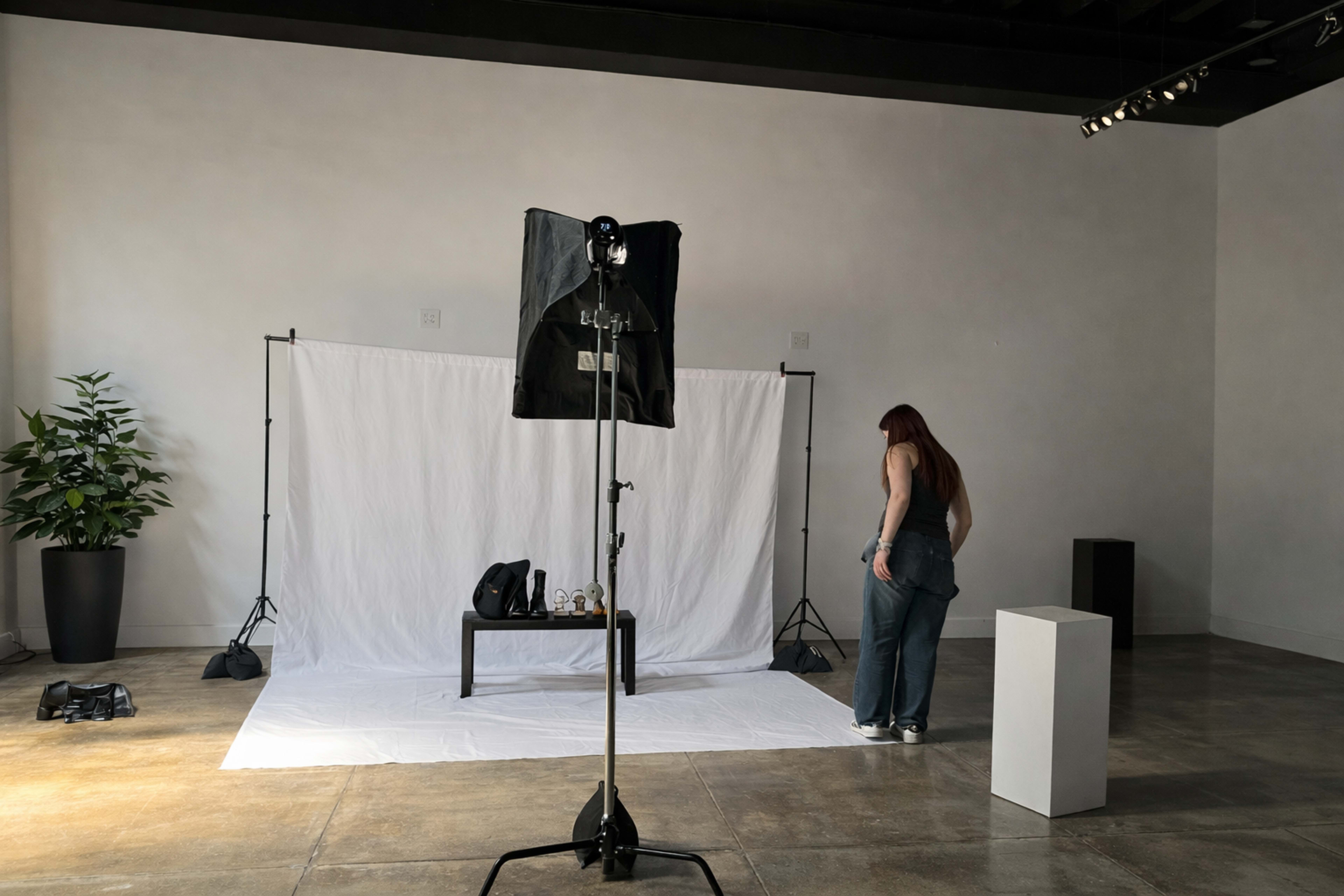 A woman stands beside a white backdrop in a spacious, well-lit photography studio.