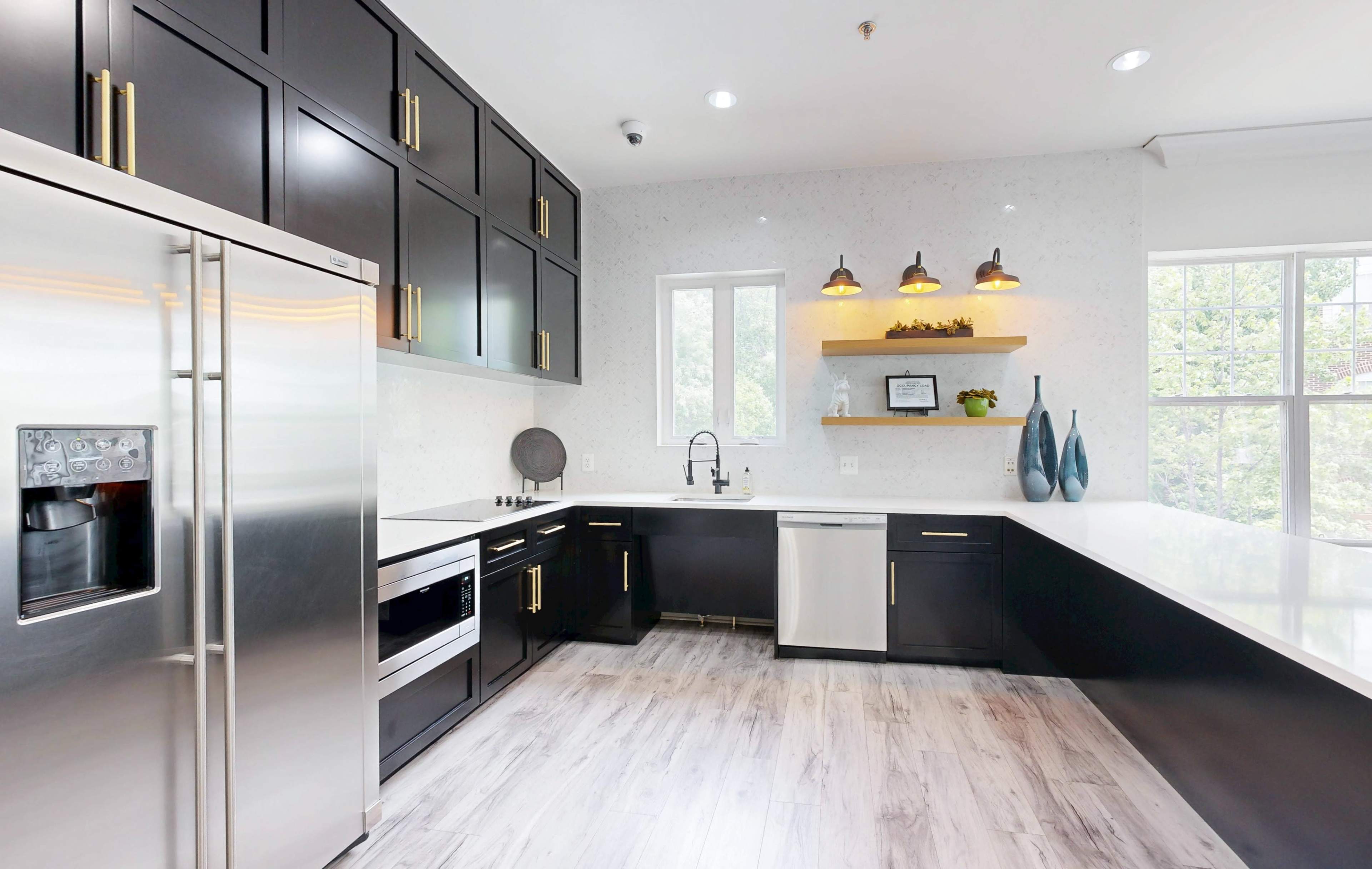 The image shows a modern kitchen featuring sleek black cabinets, stainless steel appliances, and a white countertop.