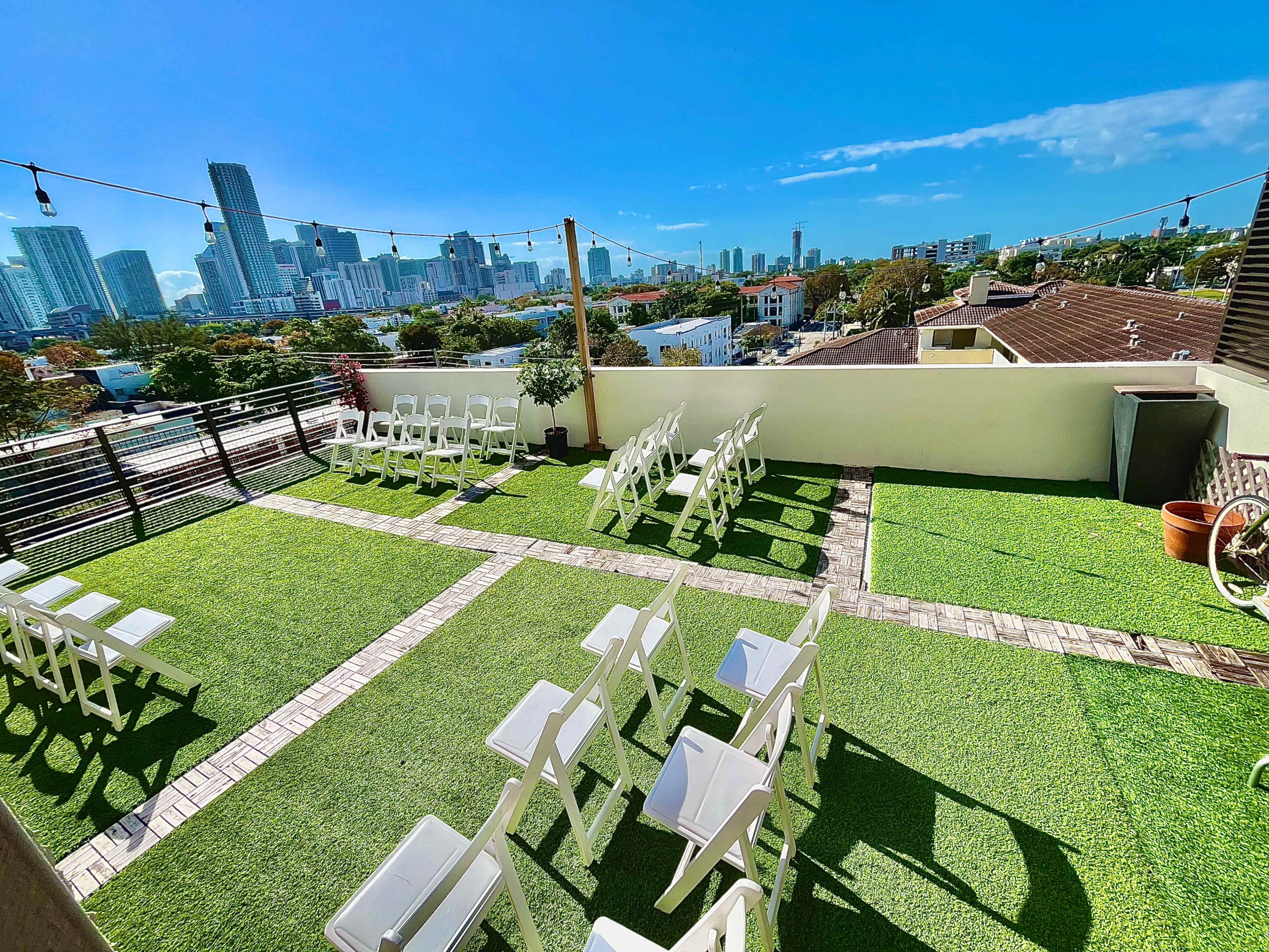 The image shows a rooftop venue set up with white chairs arranged for a ceremony, overlooking a city skyline.