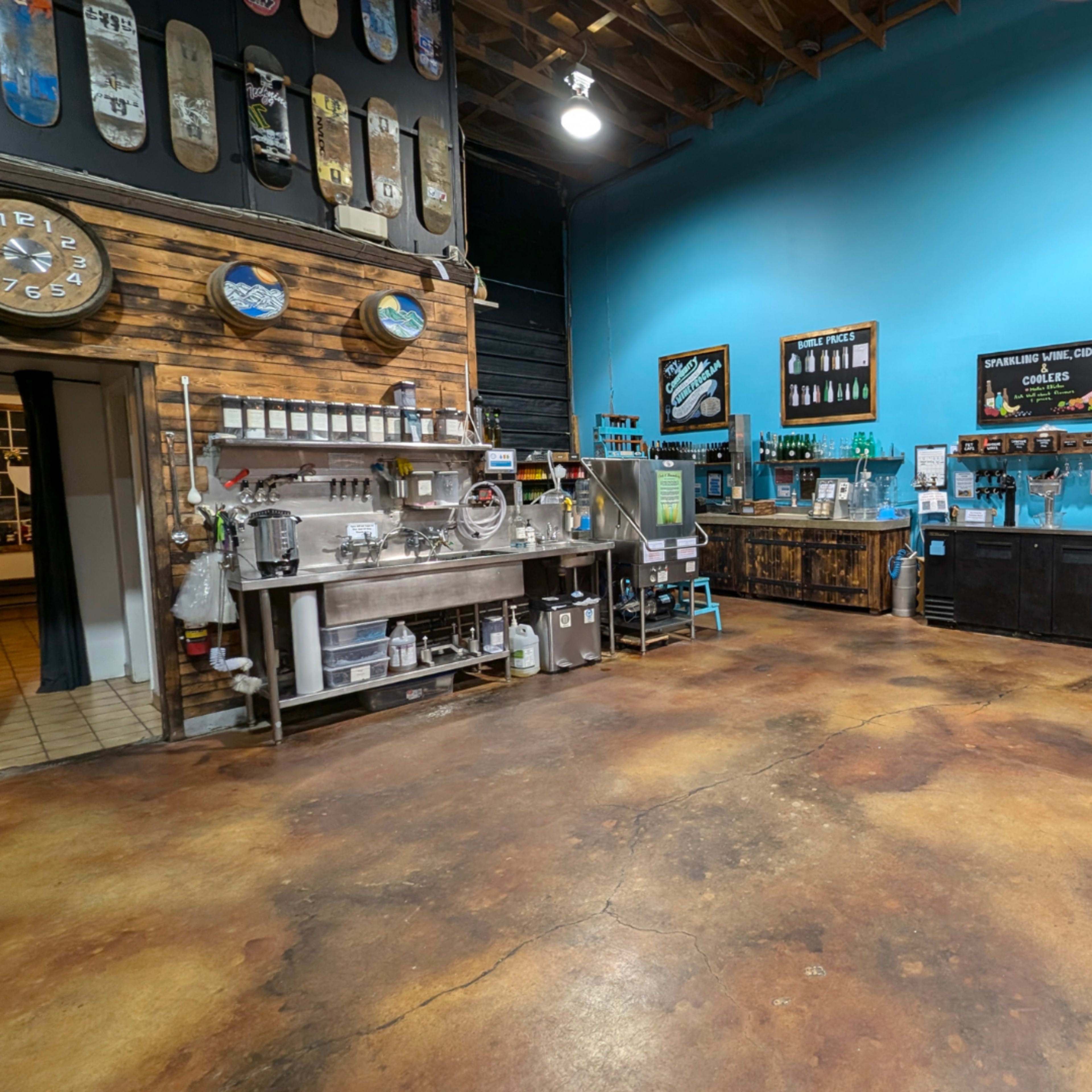 The image shows a minimalist interior of a café featuring a wooden counter, a stainless steel preparation area, and colorful skateboards mounted on the wall.