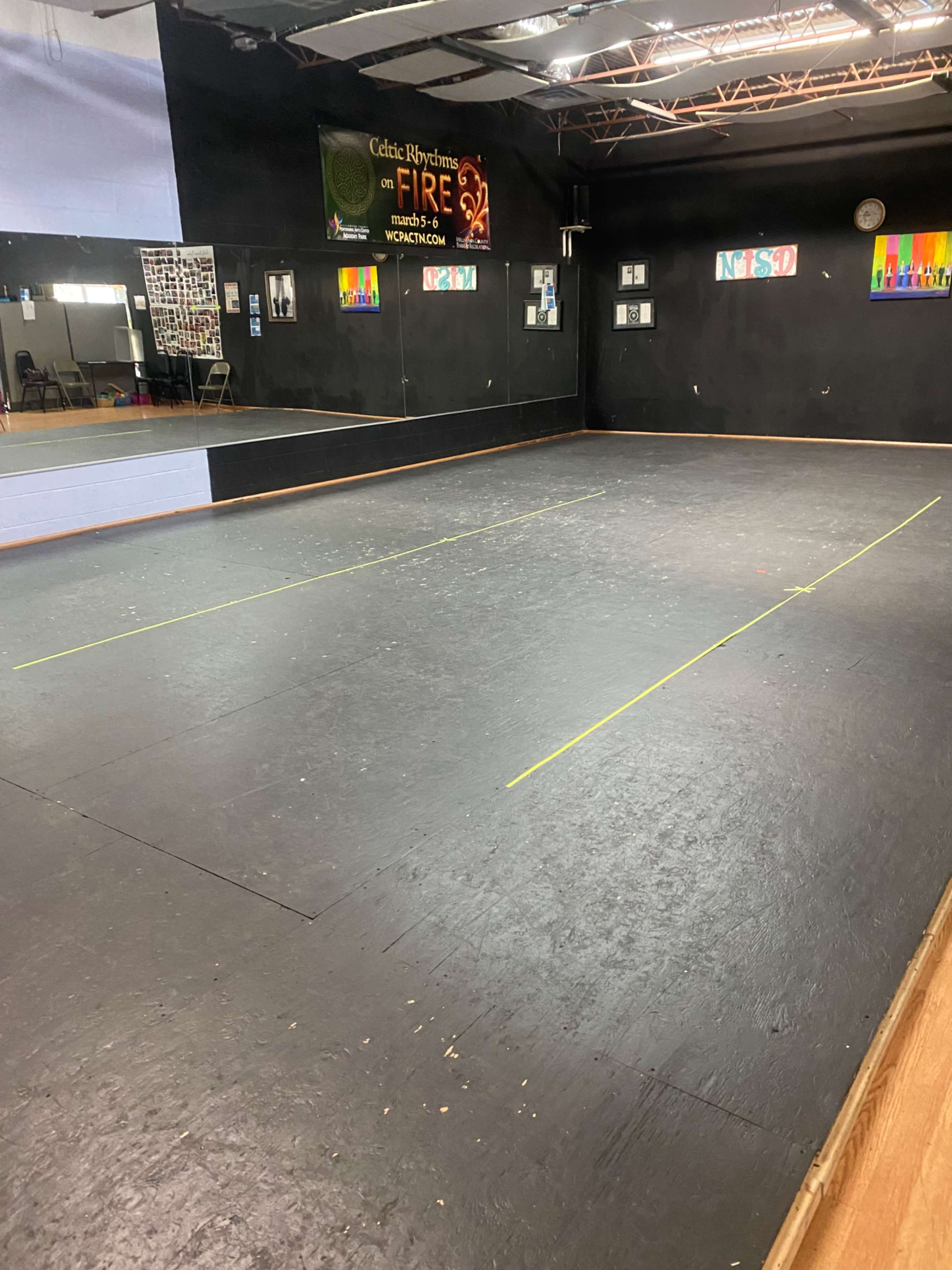 An empty dance studio with a dark floor, mirrors on the walls, and a banner hanging above.