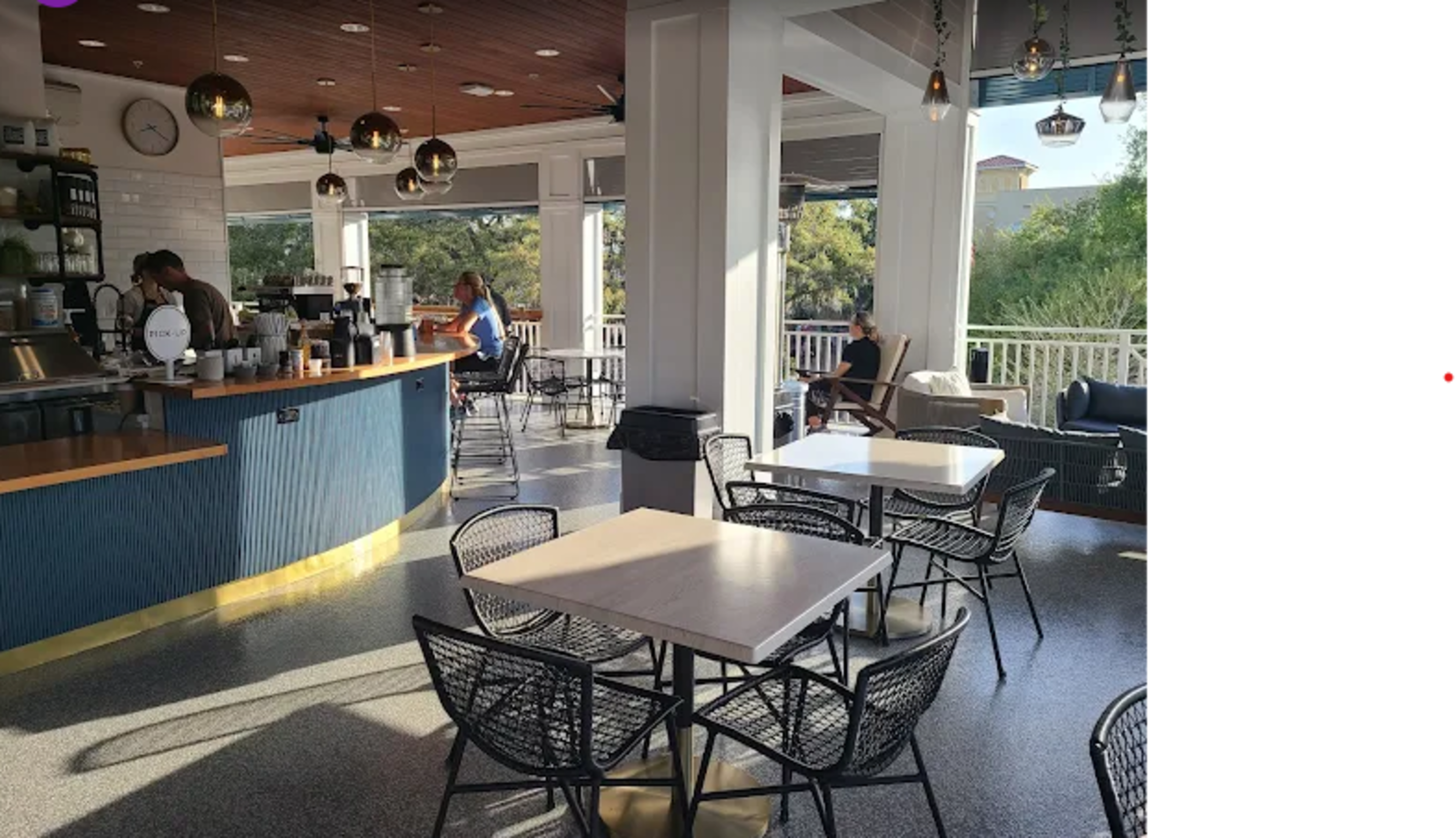 The image shows a spacious café interior with a bar counter, several tables, and chairs arranged in a well-lit area.
