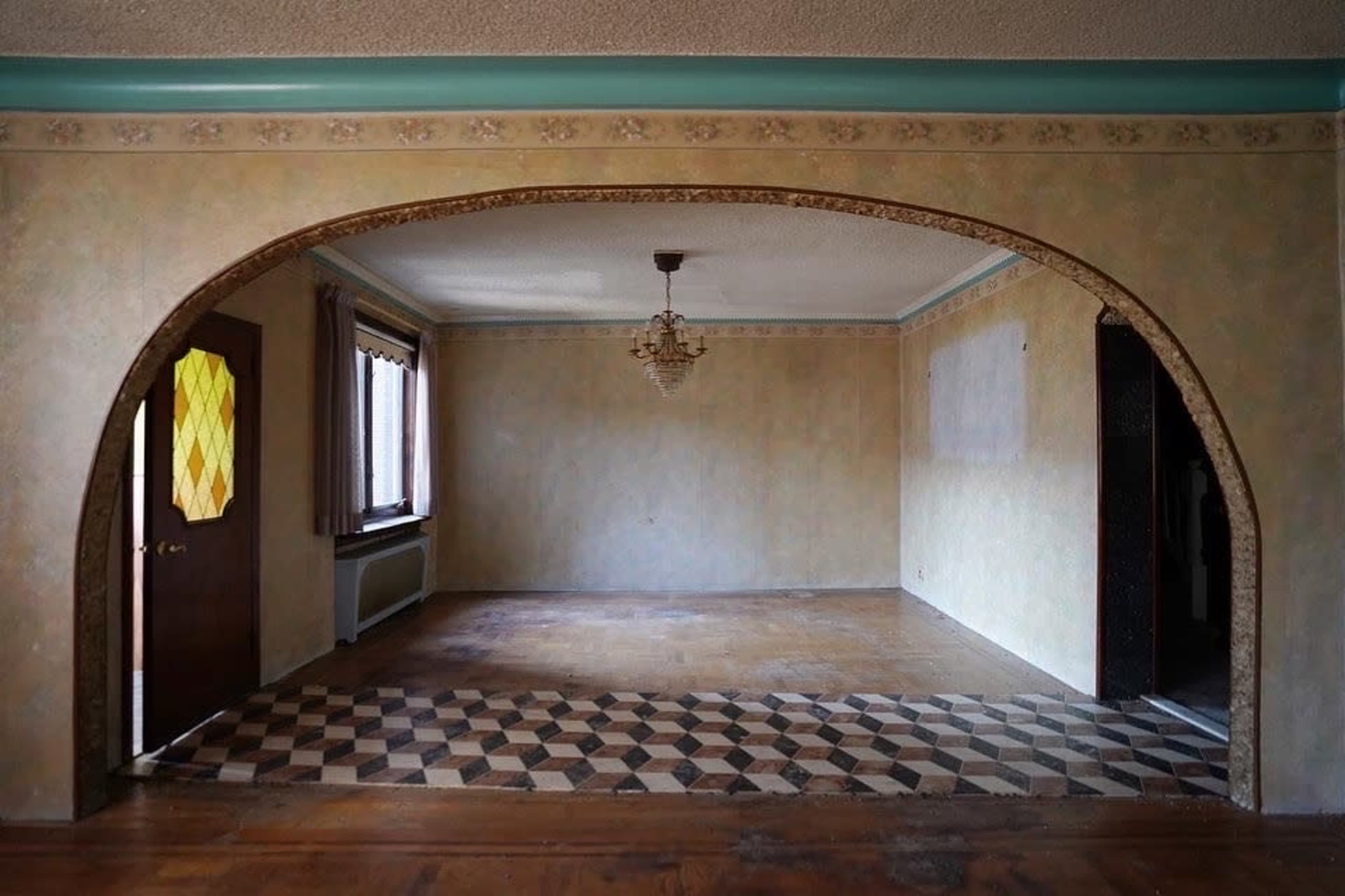 A spacious interior room with an arched entryway, featuring patterned tile flooring and beige walls.