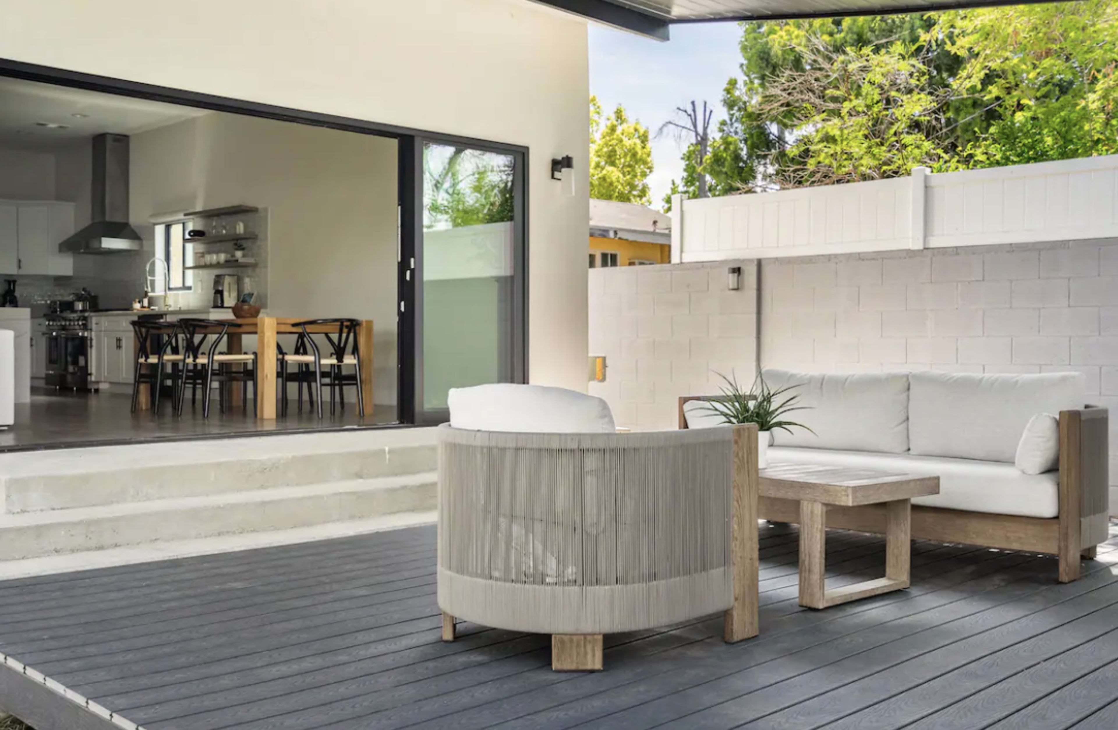 A modern outdoor seating area features a round chair and a coffee table on a wooden deck, with a view into an open kitchen and dining space.