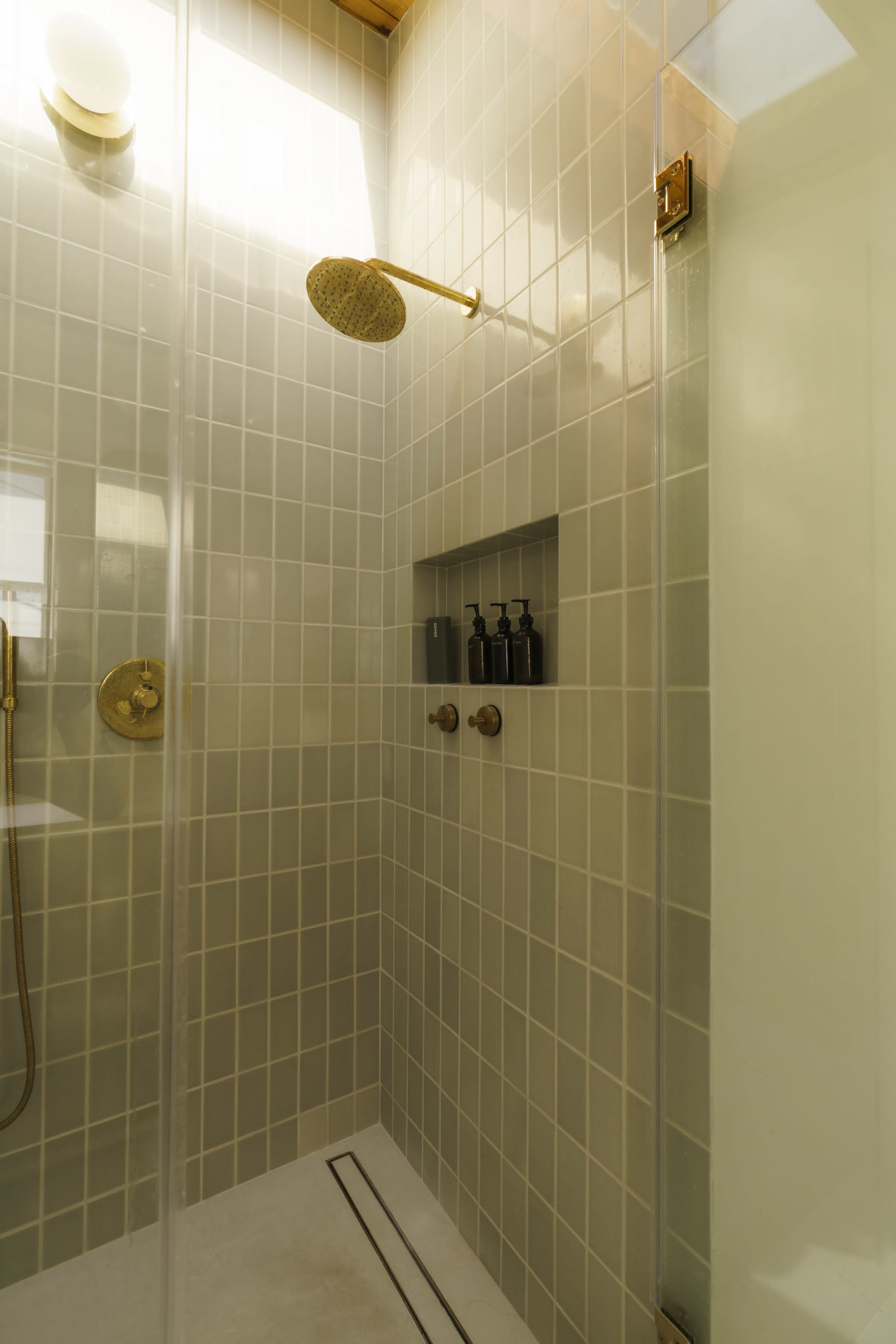 A modern shower features tiled walls, a overhead rainfall showerhead, and a built-in niche with bottles.