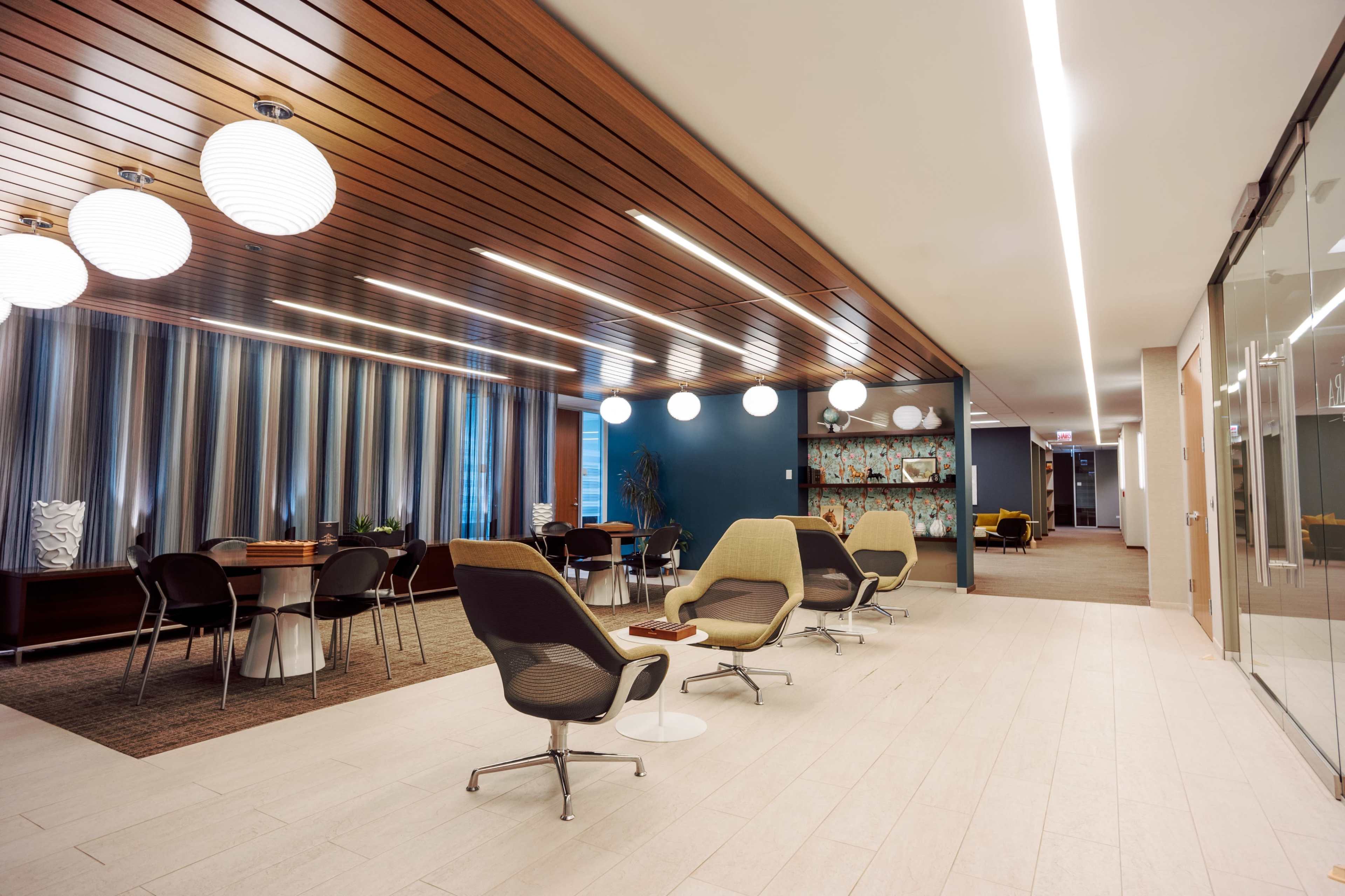 The image shows a modern office lounge area with stylish seating, decorative lighting, and a partitioned workspace in the background.
