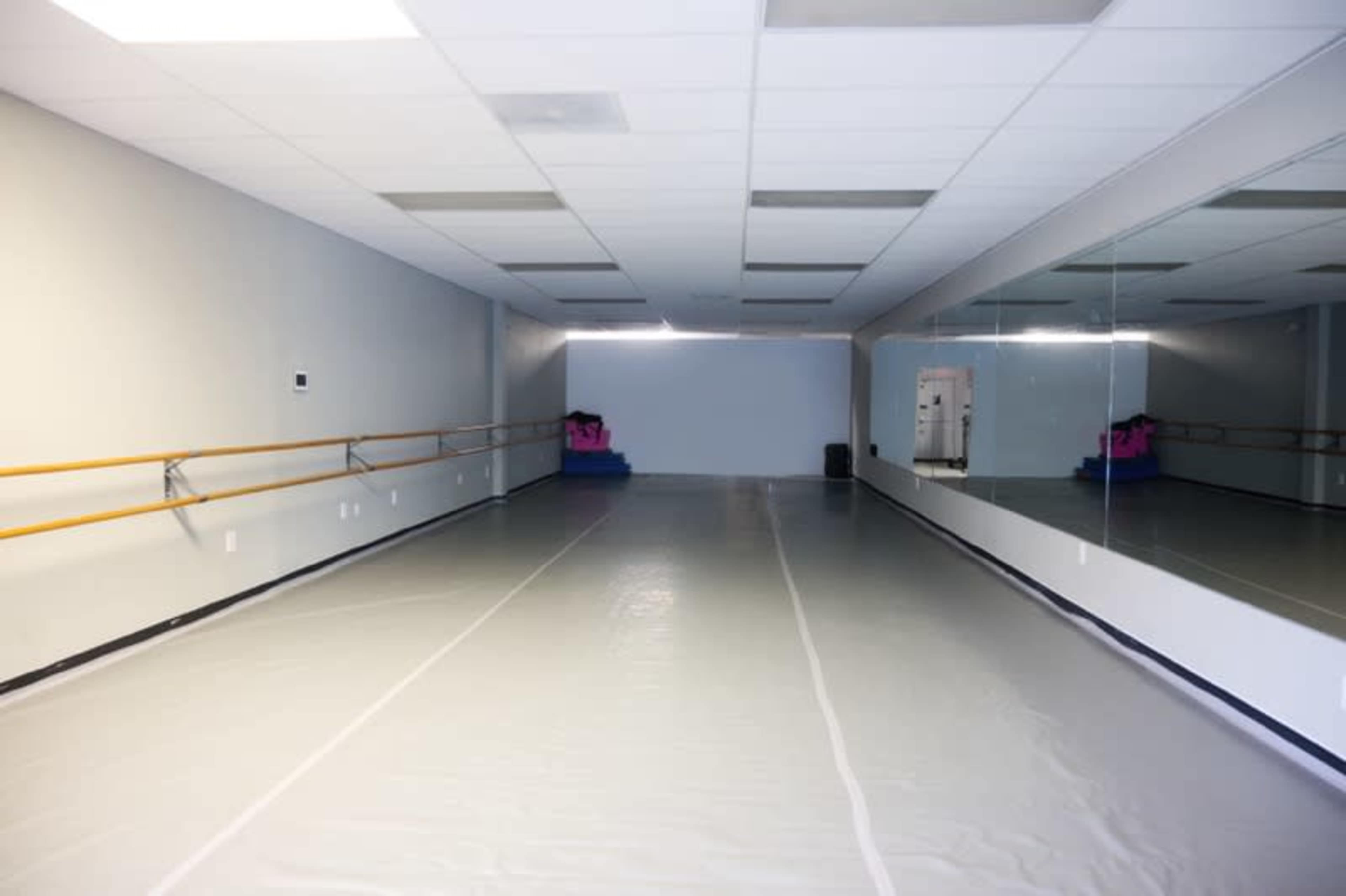 A spacious dance studio with mirrored walls and a smooth floor, illuminated by overhead lights.