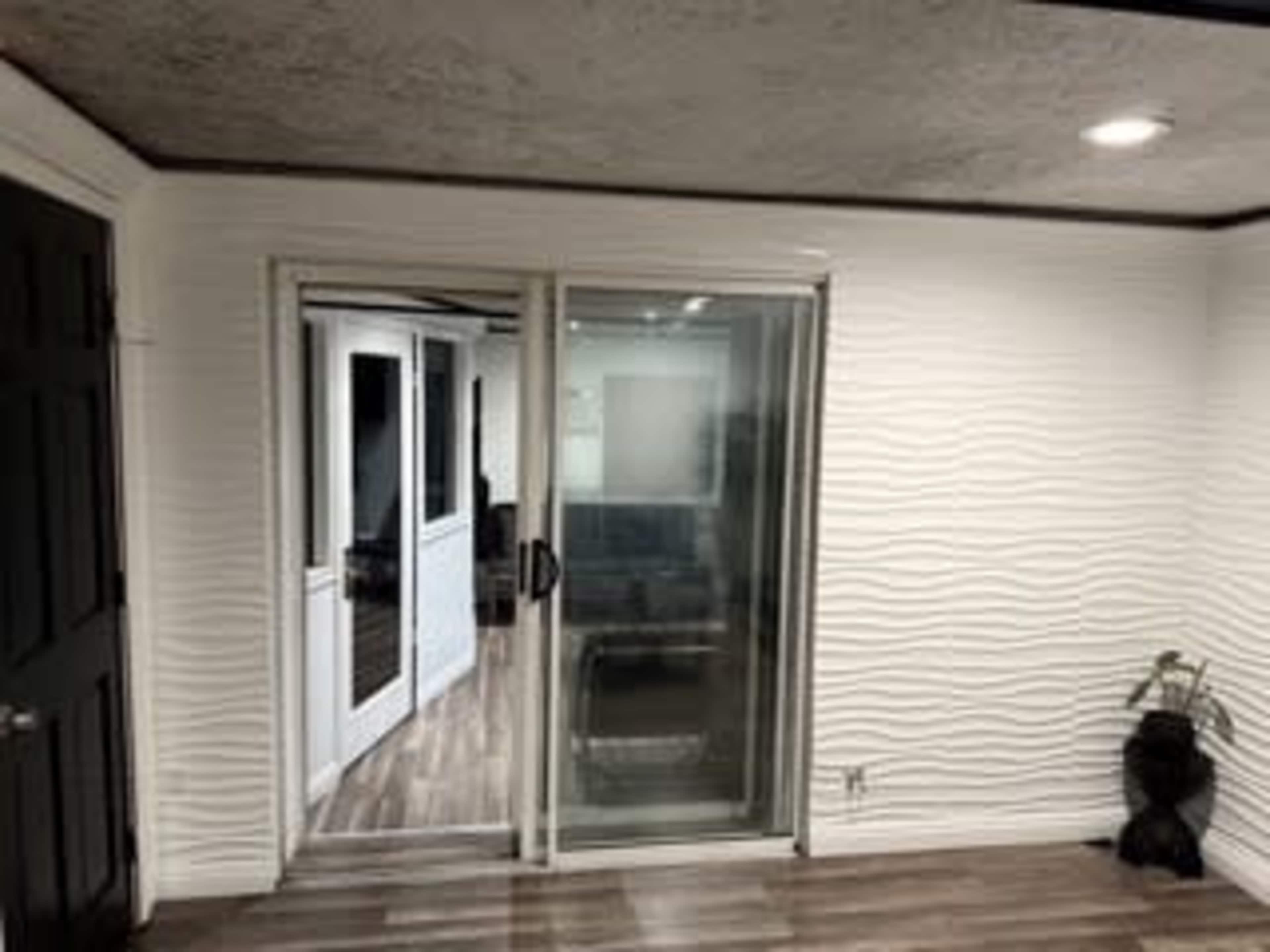 The image shows a room with a sliding glass door leading to another area, featuring textured white walls and wooden flooring.